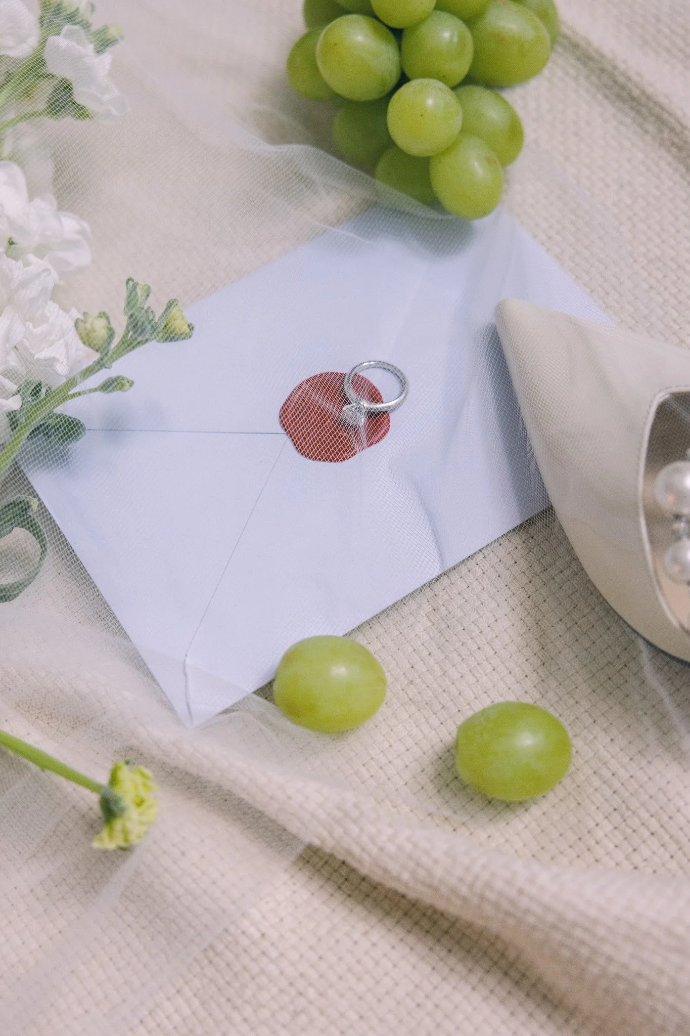 Wedding details with wedding ring, fabric, fruit, and floral styling on a soft neutral background.