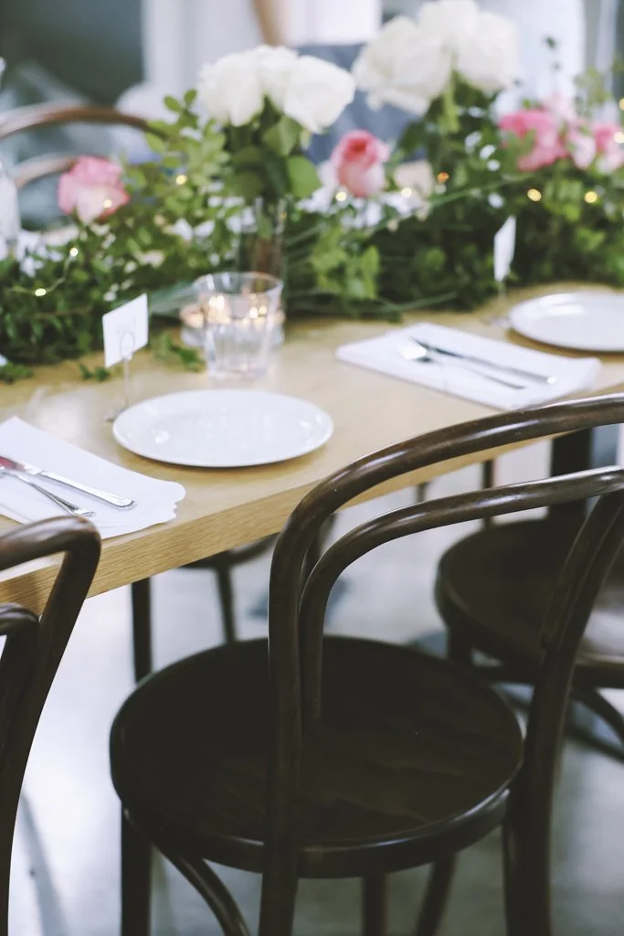 An indoor wedding reception table setting with an open-air feel, featuring neutral linens, plates, and floral details.