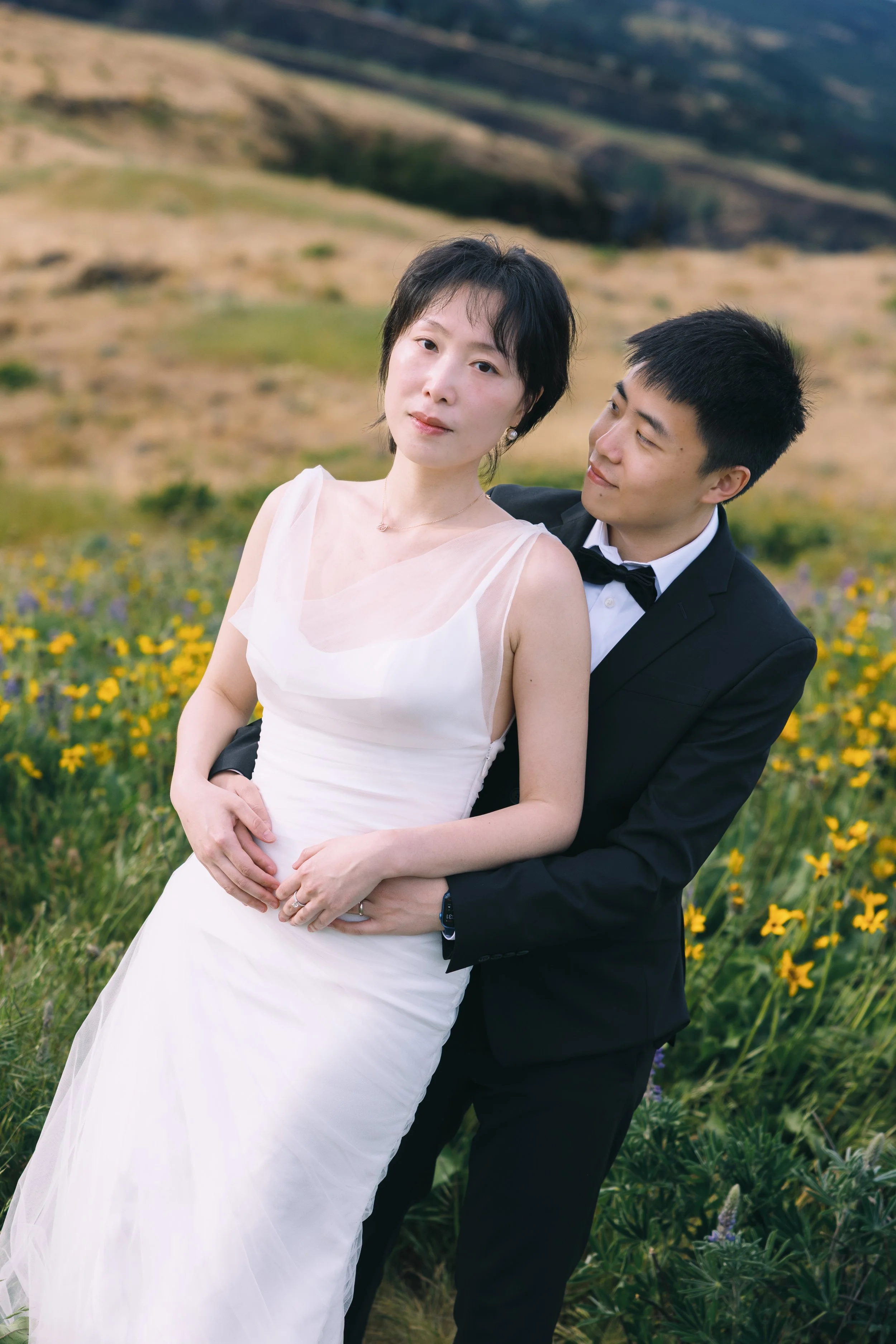 Editorial engagement portrait of a couple surrounded by yellow wildflowers and rolling hills.