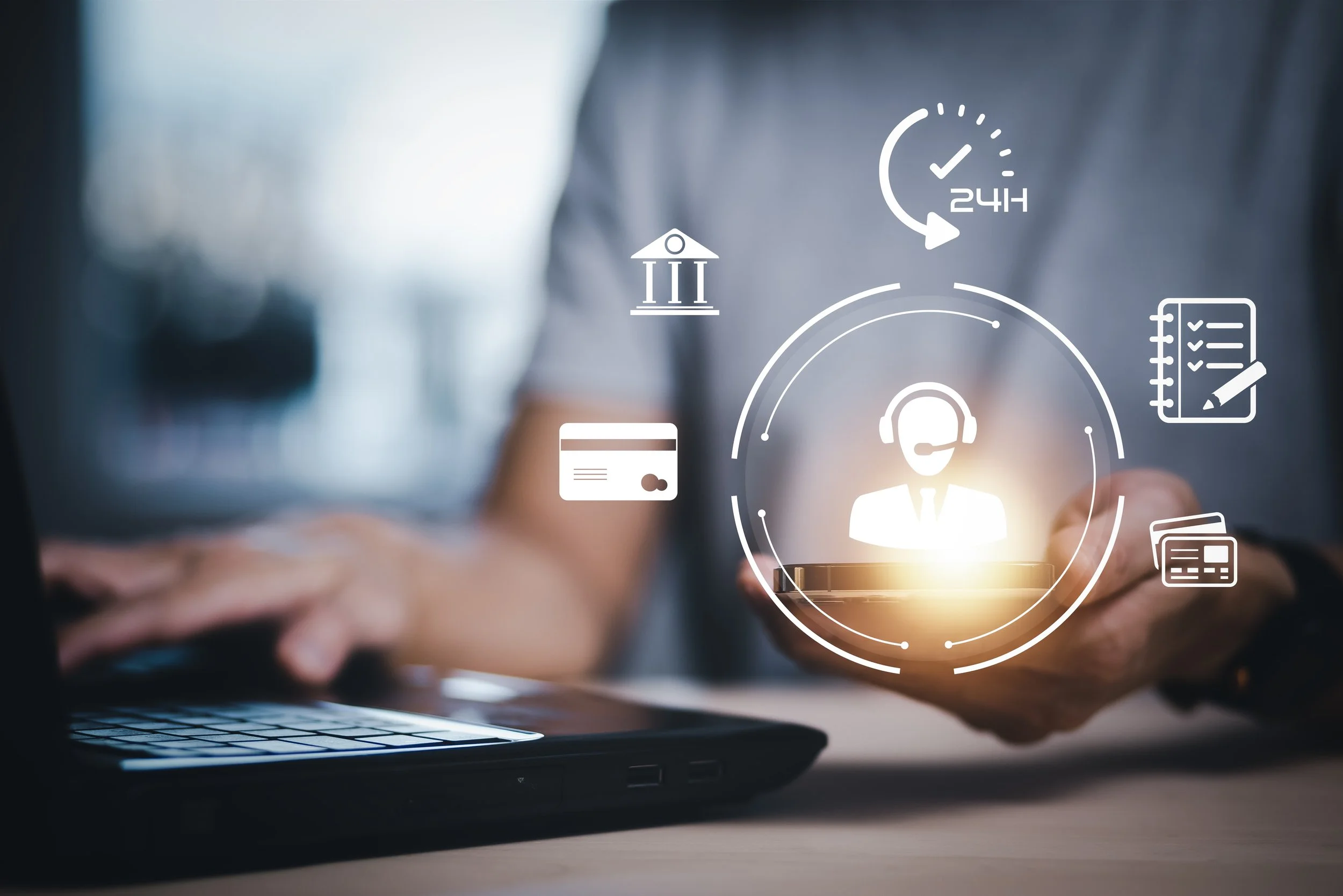 Person holding a smartphone with digital icons related to customer service, banking, and 24-hour support floating above, while working on a laptop.