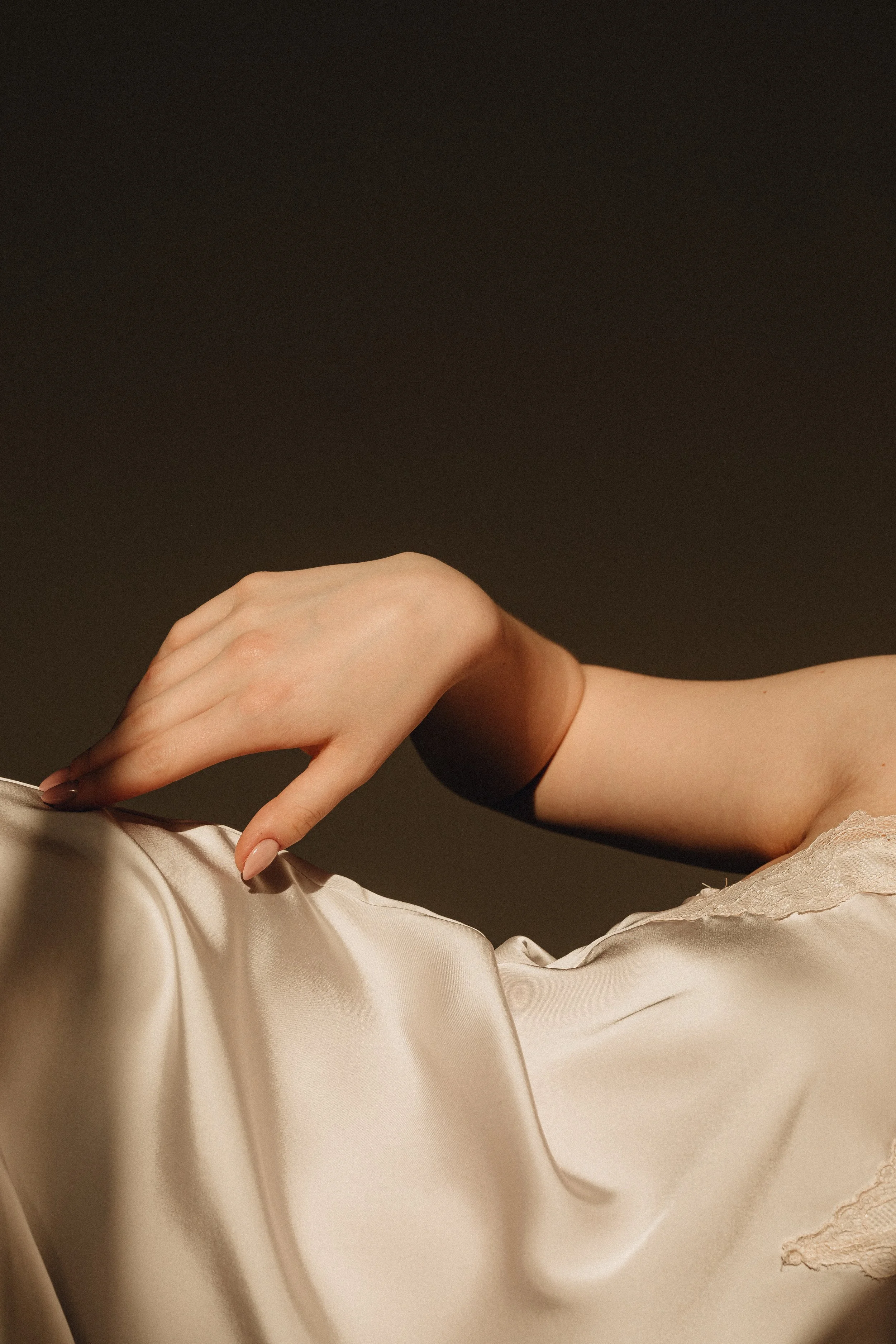 Soft feminine hand touching flowing beige satin under warm light, elegant and intimate atmosphere.