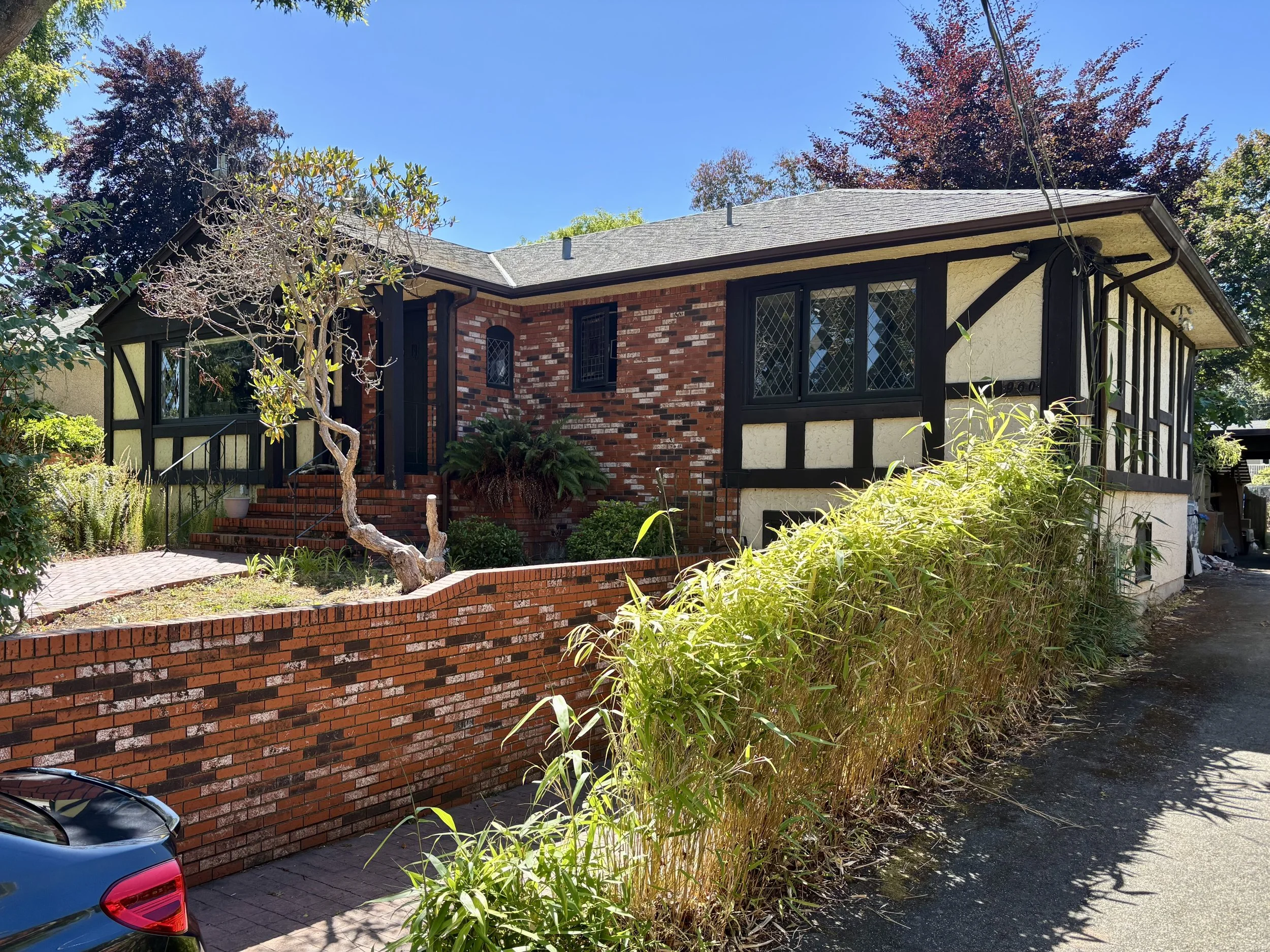 Suburban house with a brick and half-timbered facade, front steps, garden, and driveway, under a blue sky. 5-MeO-DMT Ceremony Retreat Facilitator British Columbia Canada