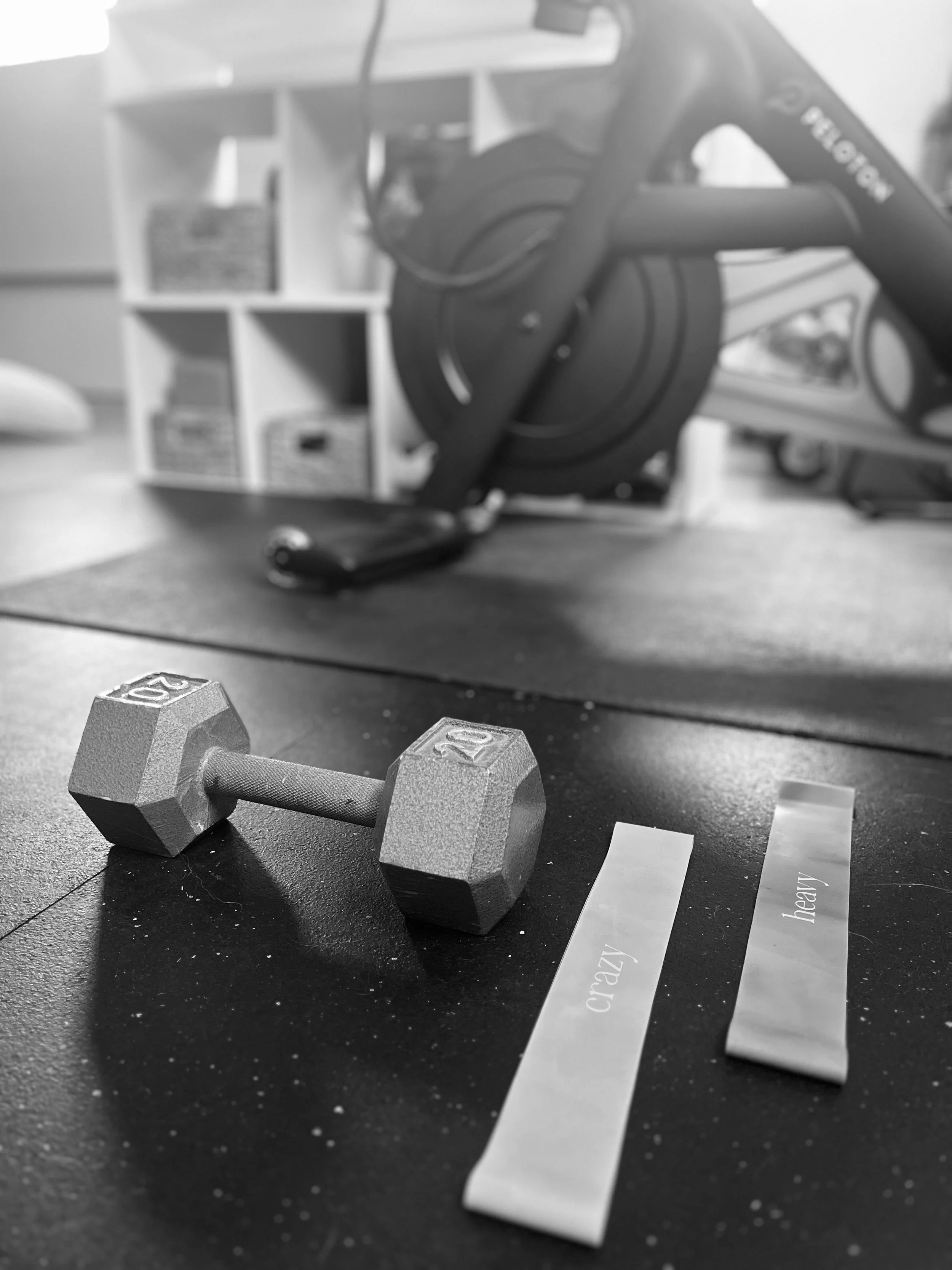 A small white computer keyboard and a measuring tape on a table, with a protractor and a ruler nearby; in the background, exercise equipment and a white shelf with potted plants and baskets.