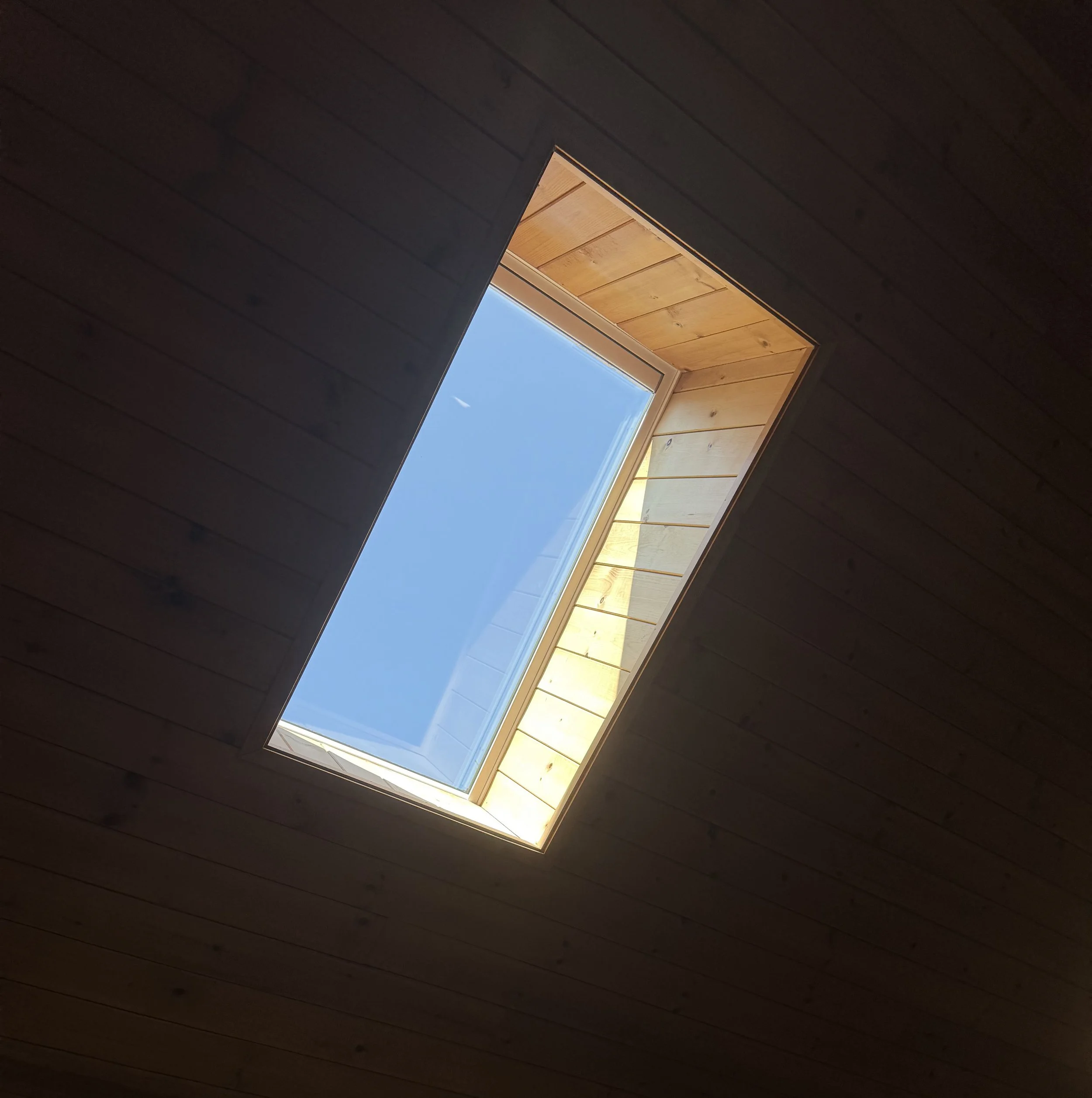 Looking up through a square opening in a wooden ceiling, blue sky visible outside.