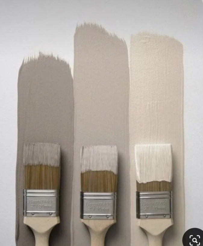Three paintbrushes with different shades of beige paint on wall behind them, illustrating paint color gradient.