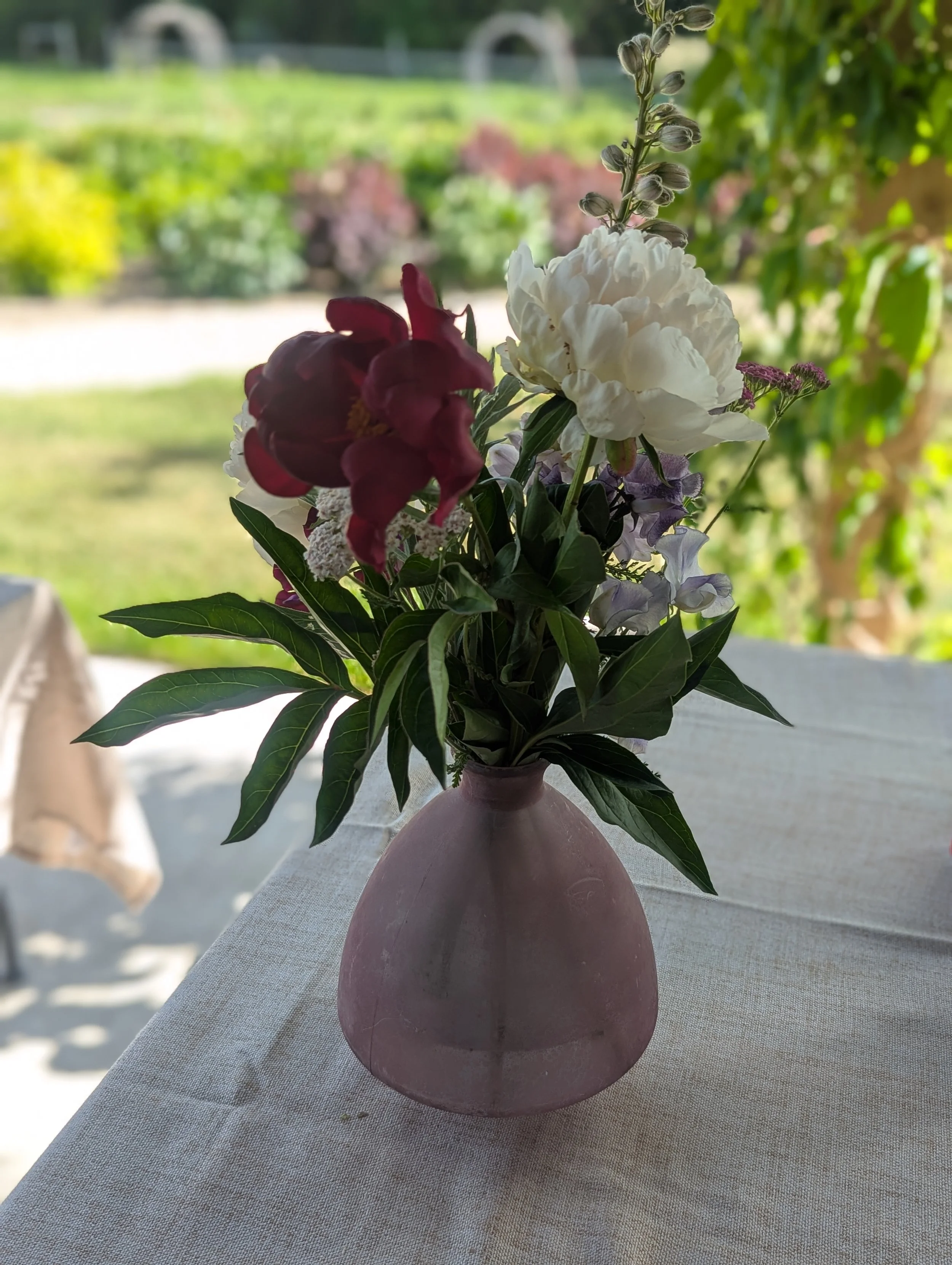 A bouquet of mixed flowers in a pink vase on a table outdoors with a blurred garden background.