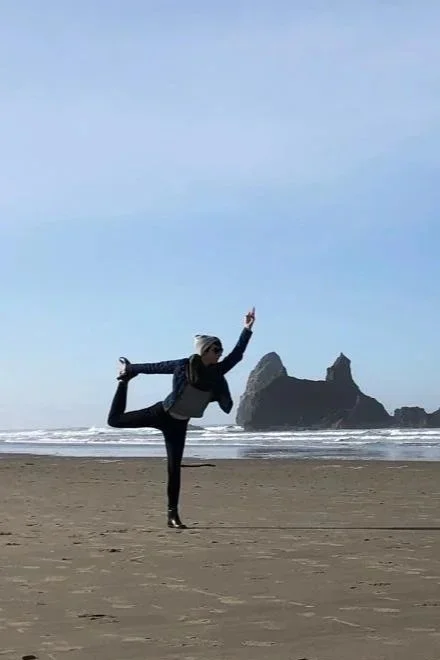 Person practicing yoga on a beach with rock formations in the background.