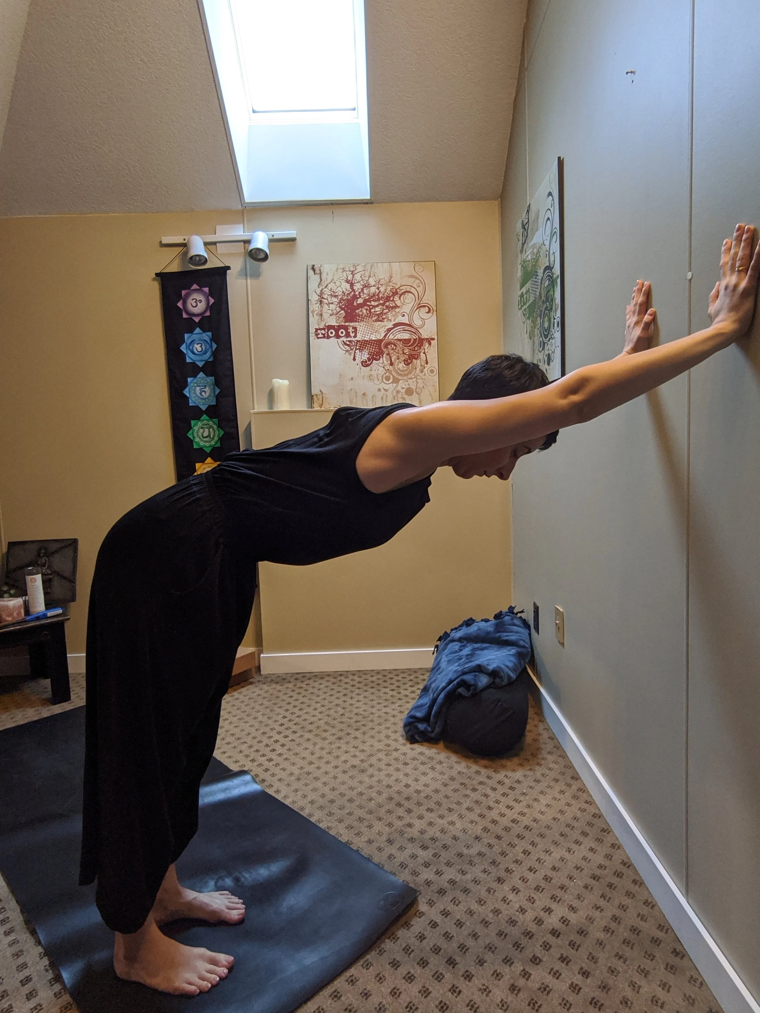 Person practicing yoga in a wall stretch leaning forward on a yoga mat in a room with spiritual decor and artwork.