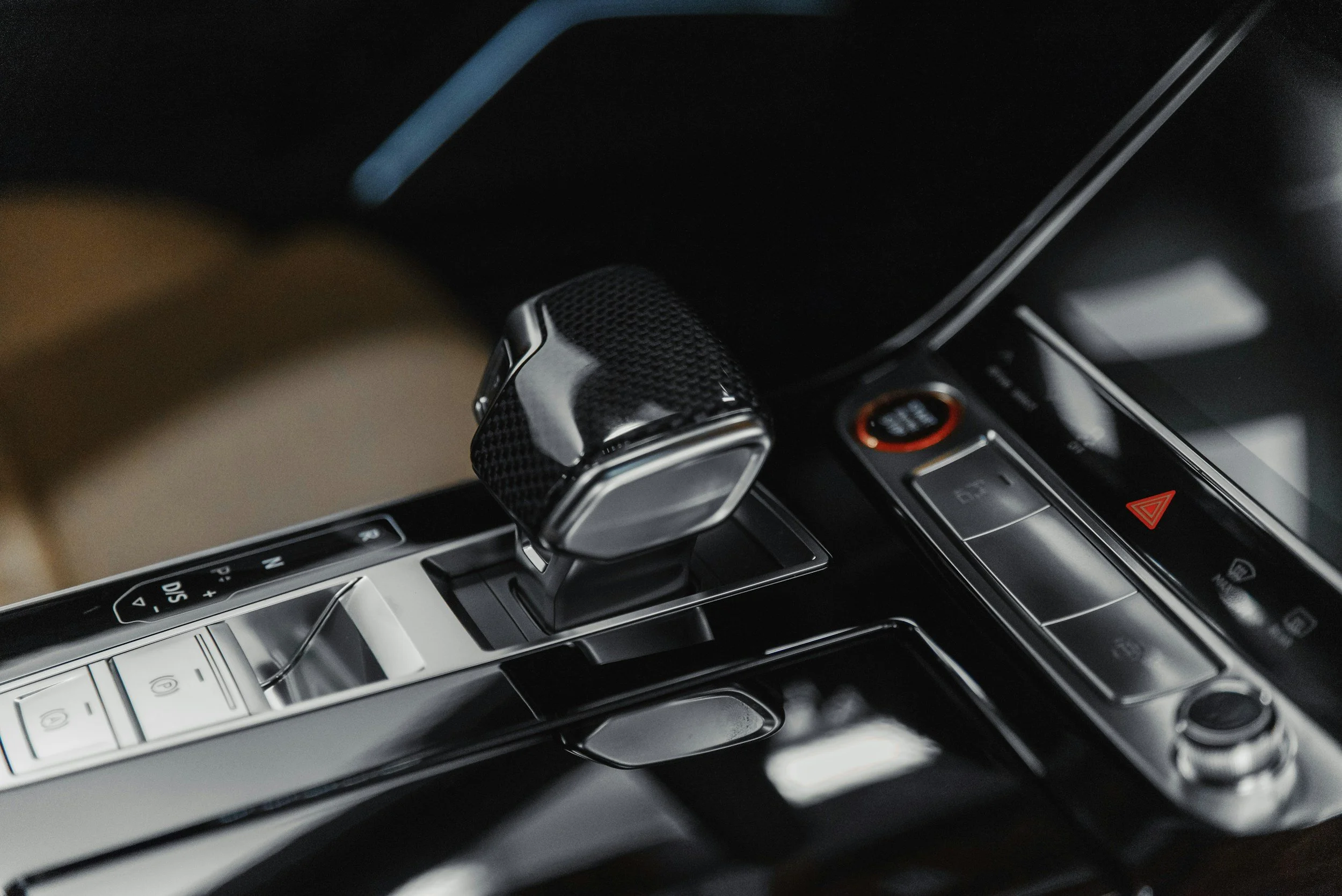 Close-up of a luxurious car interior showing a gear shifter with a carbon fiber finish and modern control buttons.