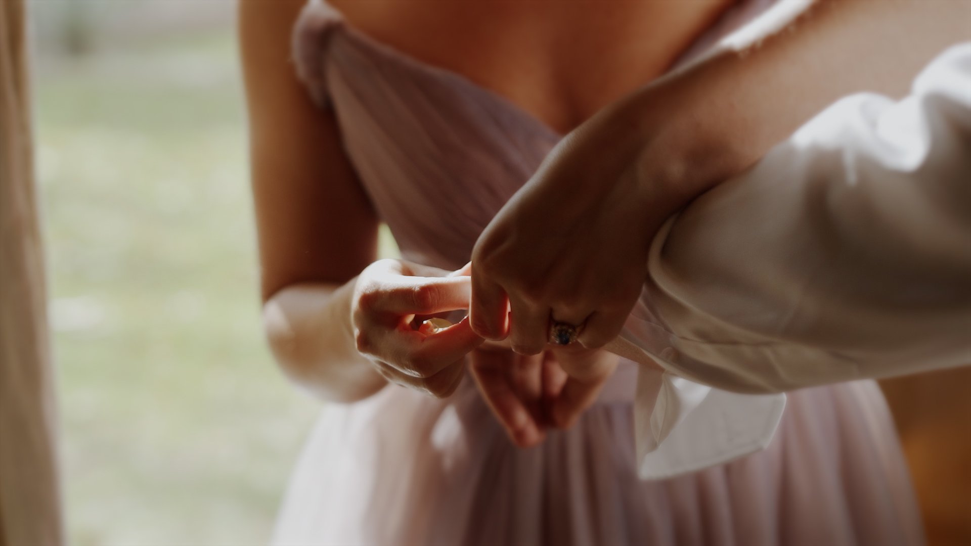 Couple walking arm-in-arm down a grassy aisle during their outdoor wedding ceremony, surrounded by friends throwing leaves and confetti, with a decorative wooden backdrop and green mountains in the background.