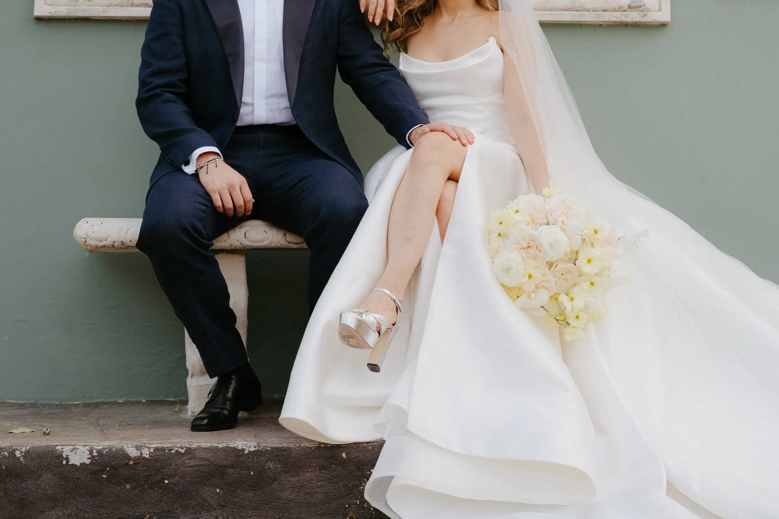 Wedding reception outdoor setup with a long table decorated with white linens and greenery, hanging paper lanterns, string lights, and lanterns on the ground surrounded by trees.
