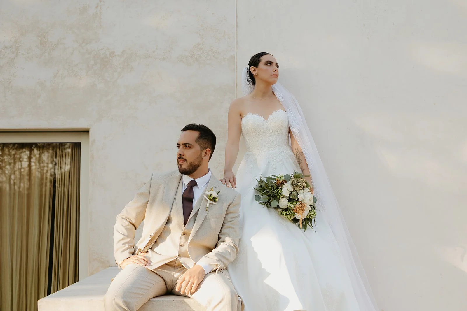 Couple walking arm-in-arm down a grassy aisle during their outdoor wedding ceremony, surrounded by friends throwing leaves and confetti, with a decorative wooden backdrop and green mountains in the background.