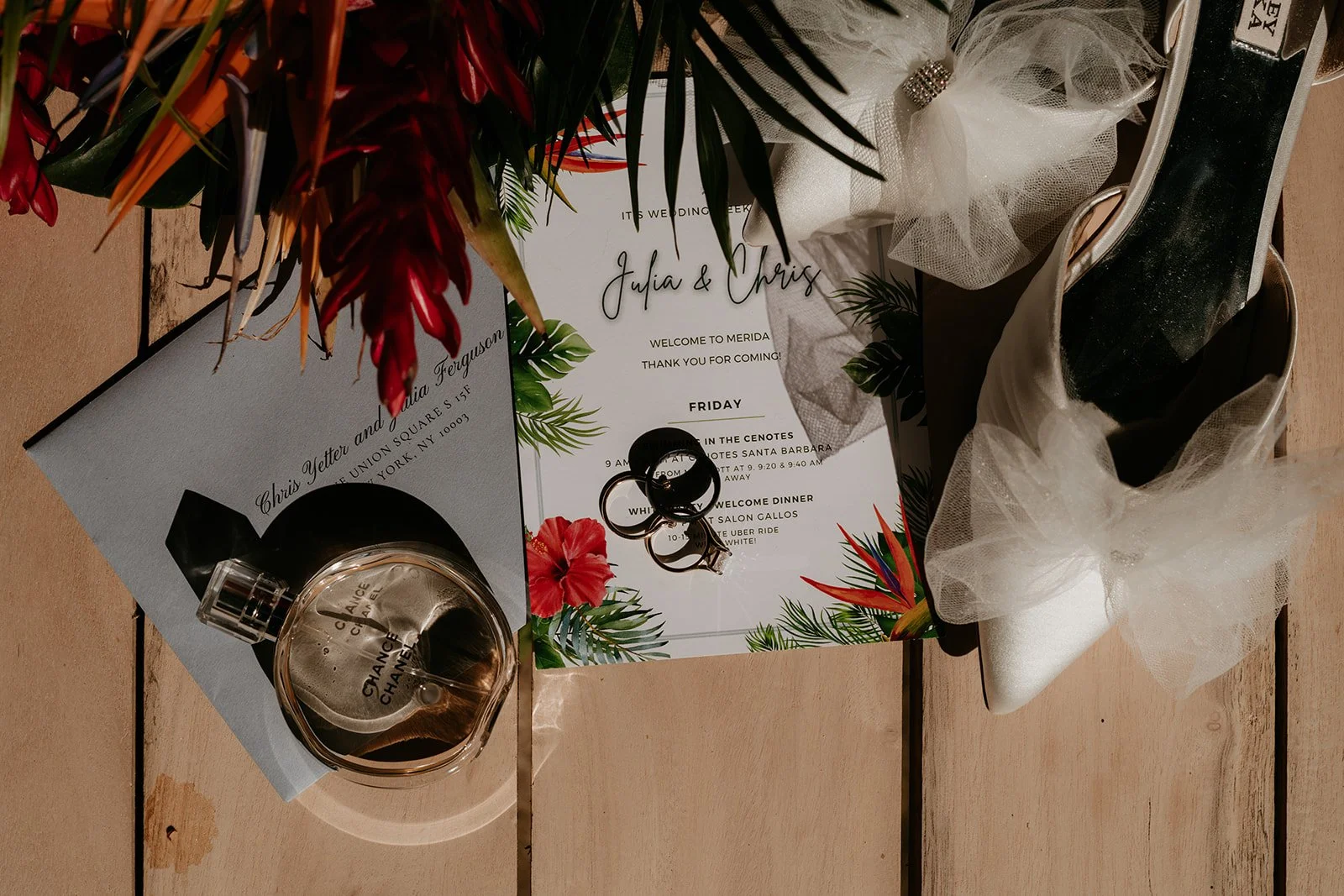 Outdoor wedding ceremony setup with a floral arch against a red wooden fence, white chairs arranged on green grass.
