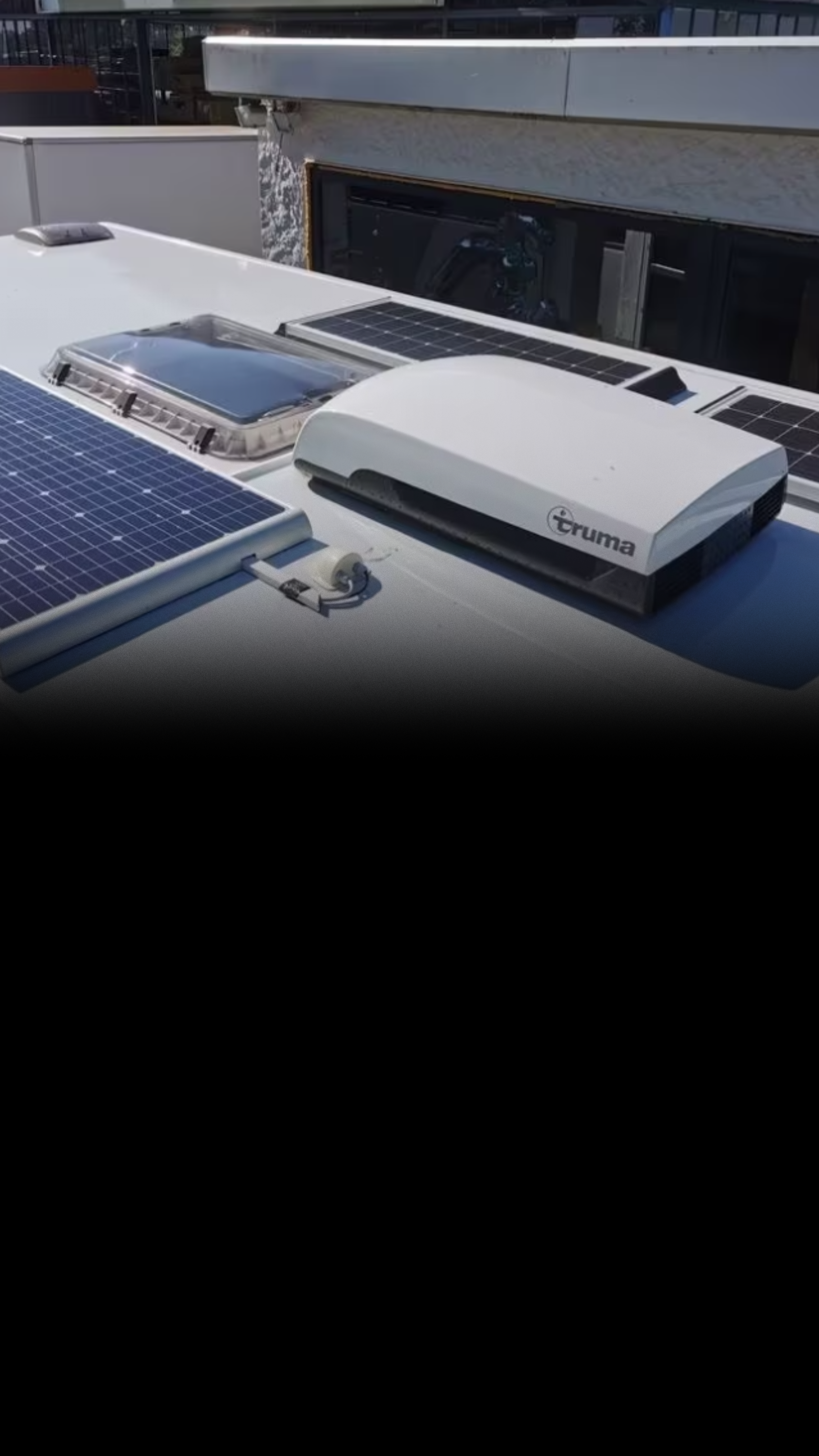 Dach eines Fahrzeugs mit Solarpanelen, einem Truma-Gerät und einem Dachlukenfenster.