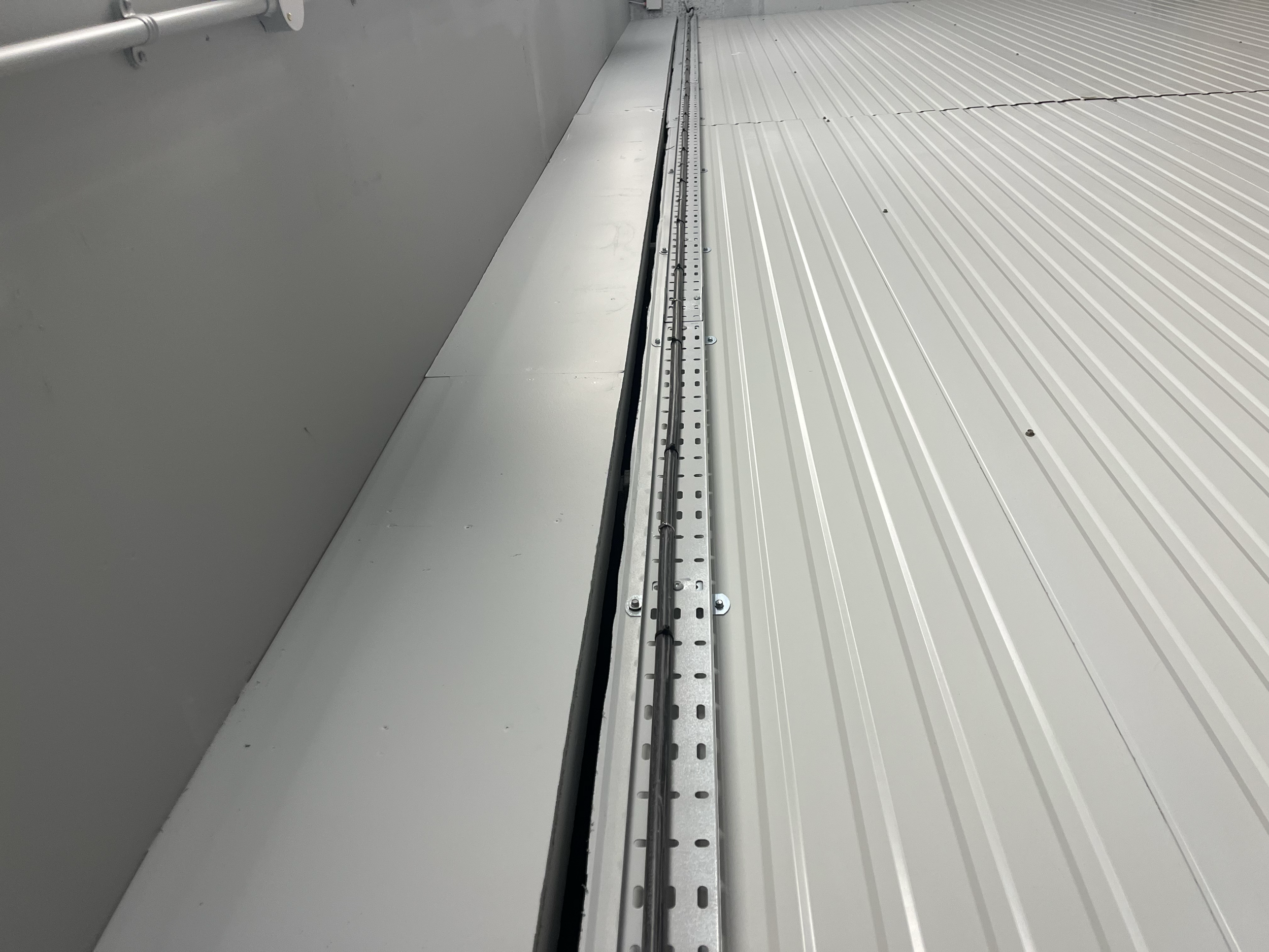A metallic overhead rail system installed along a white wall with ribbed white metal panels.
