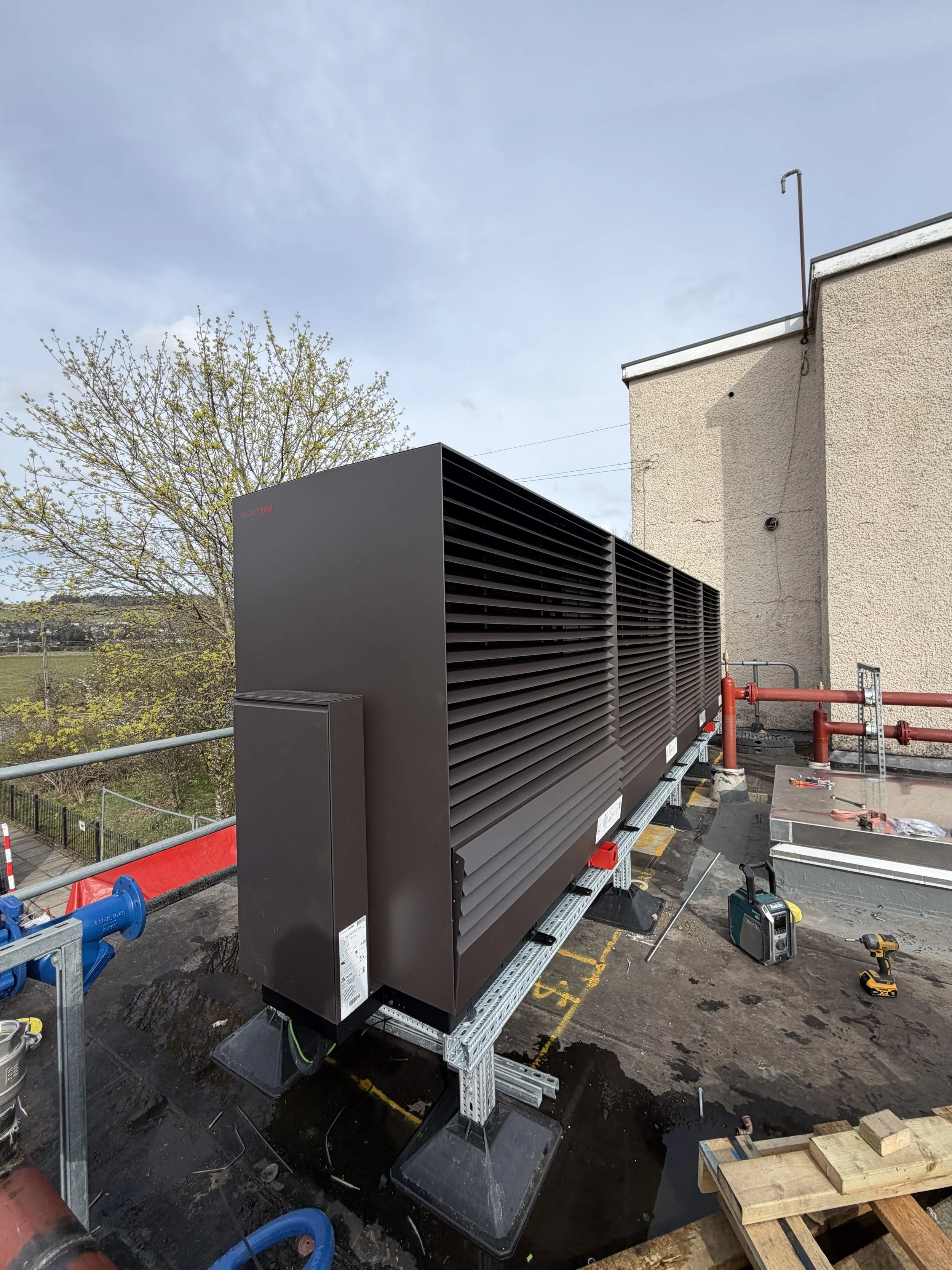 Construction site on a rooftop with large black ventilation units, tools, and safety equipment.