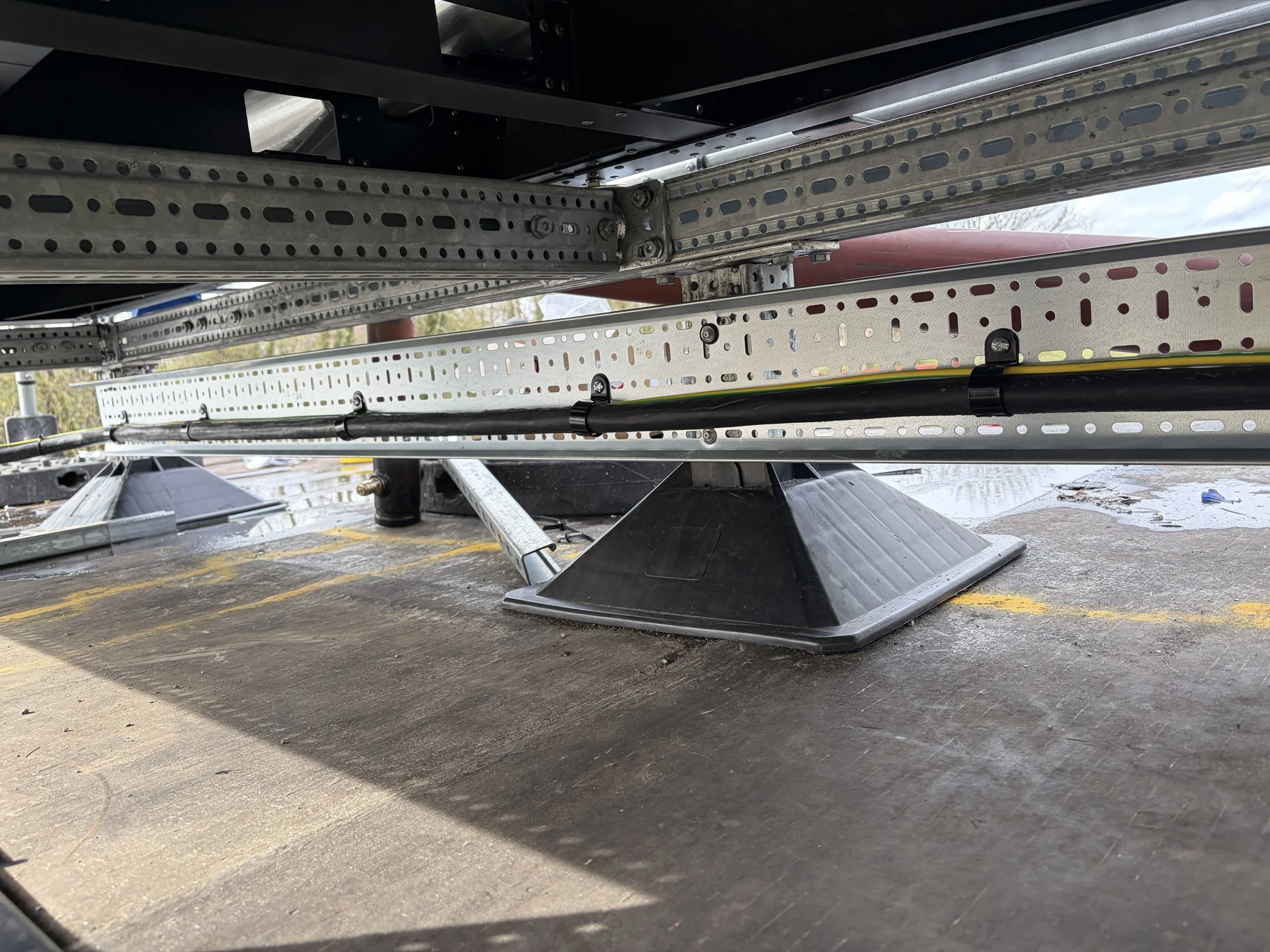 Close-up view of metal beams, bolts, and support structures under a large object or vehicle, with a wet ground surface beneath.