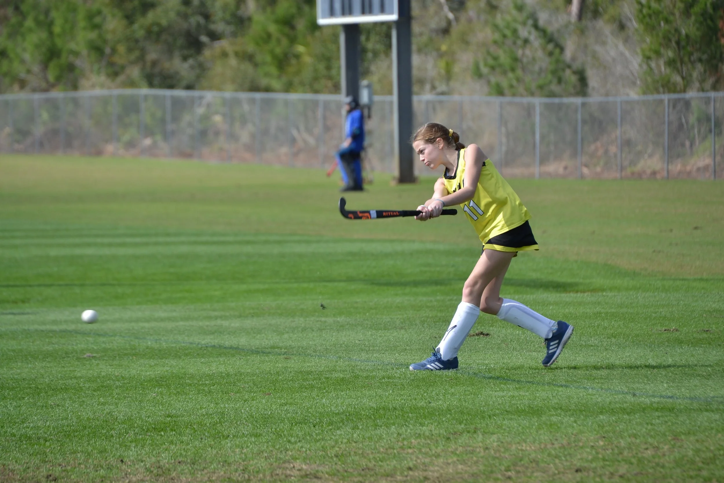 A young girl in a yellow sports uniform playing field hockey on a grassy field. Athlete and Sports Photography
