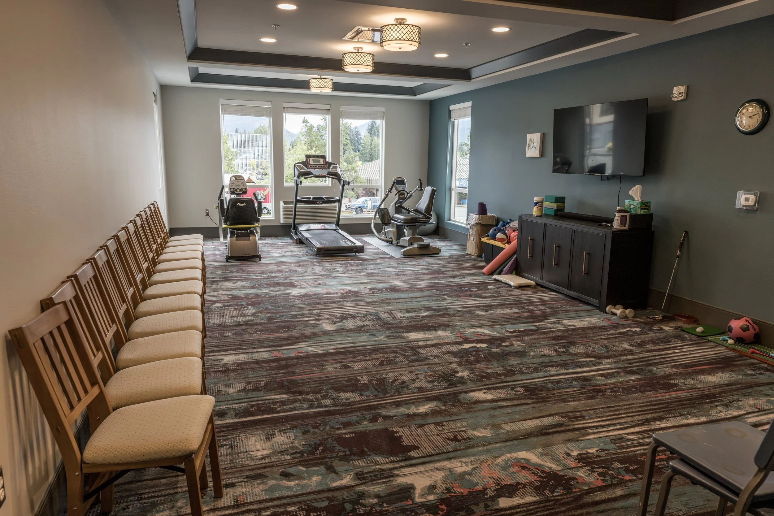 A spacious fitness room with exercise equipment including treadmills, stationary bikes, and weights at Riverview Senior Living and Memory Care in Juneau Alaska