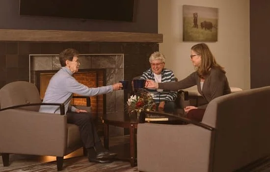Residents and visitors sitting around a coffee table in front of a fireplace at Riverview Senior Living and Memory Care in Juneau Alaska
