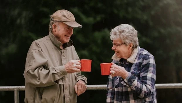 Residentshappily share coffee mugs outdoors on a railing at Riverview Senior Living and Memory Care in Juneau Alaska