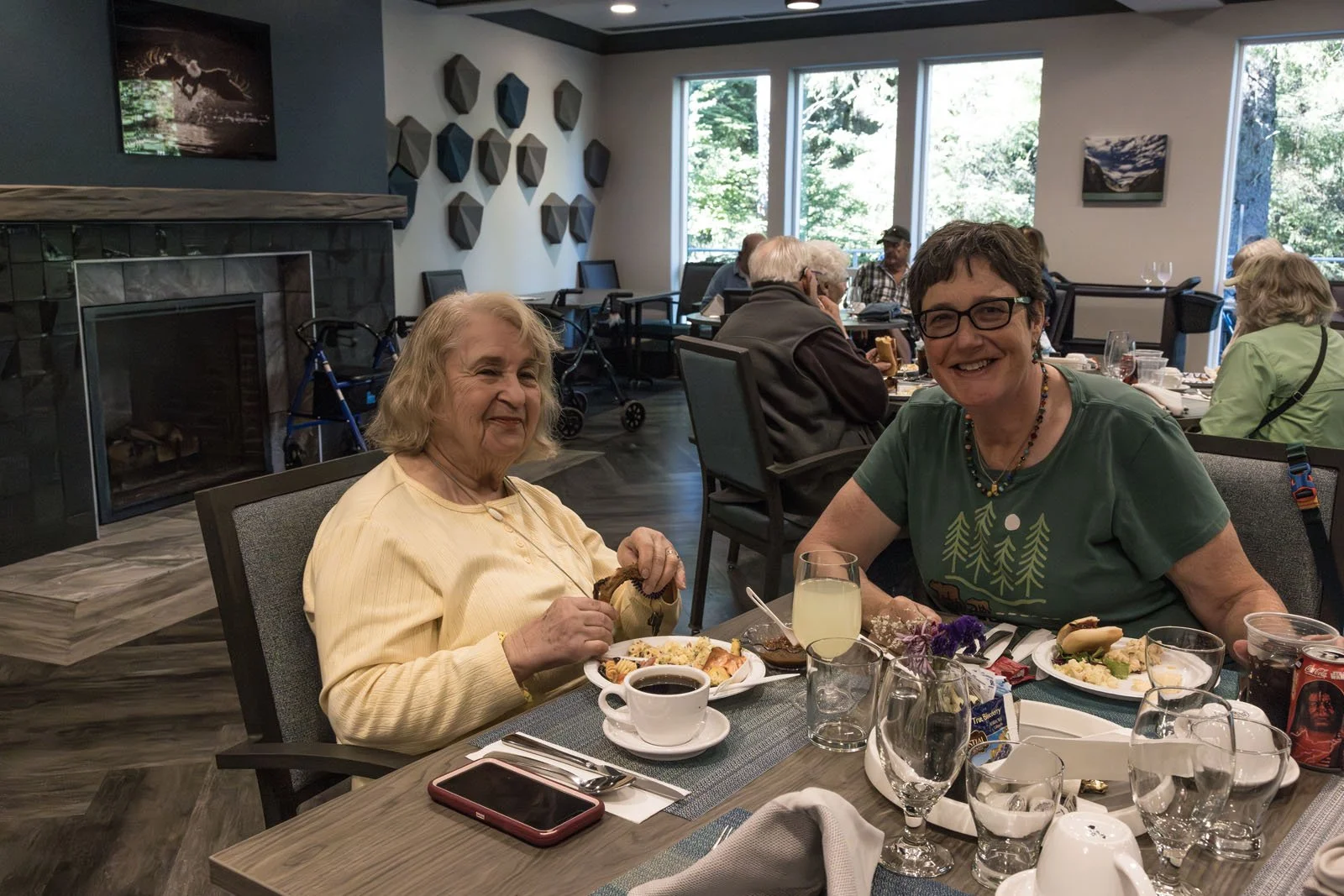 Two residents smiling at a dining table with food and drinks at Riverview Senior Living and Memory Care in Juneau Alaska