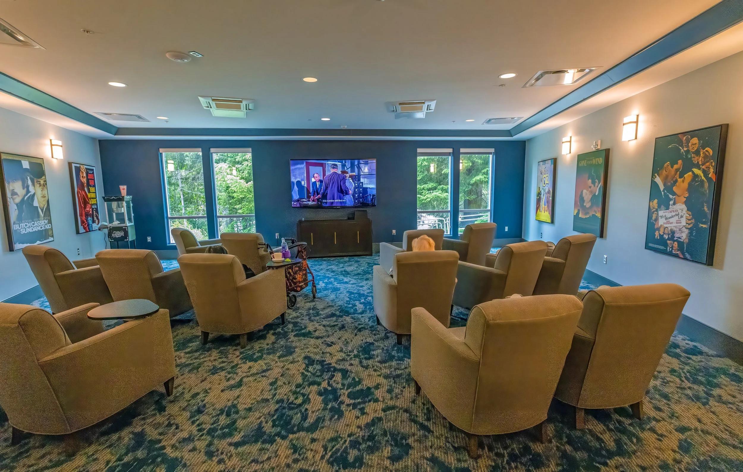 A cozy movie room with nine beige armchairs facing a large flat-screen TV at Riverview Senior Living and Memory Care in Juneau Alaska