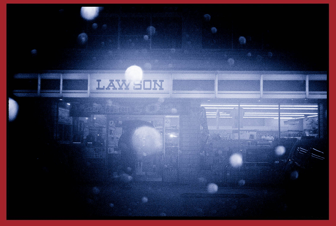 A convenience store named Lawson illuminated at night with raindrops on the window.