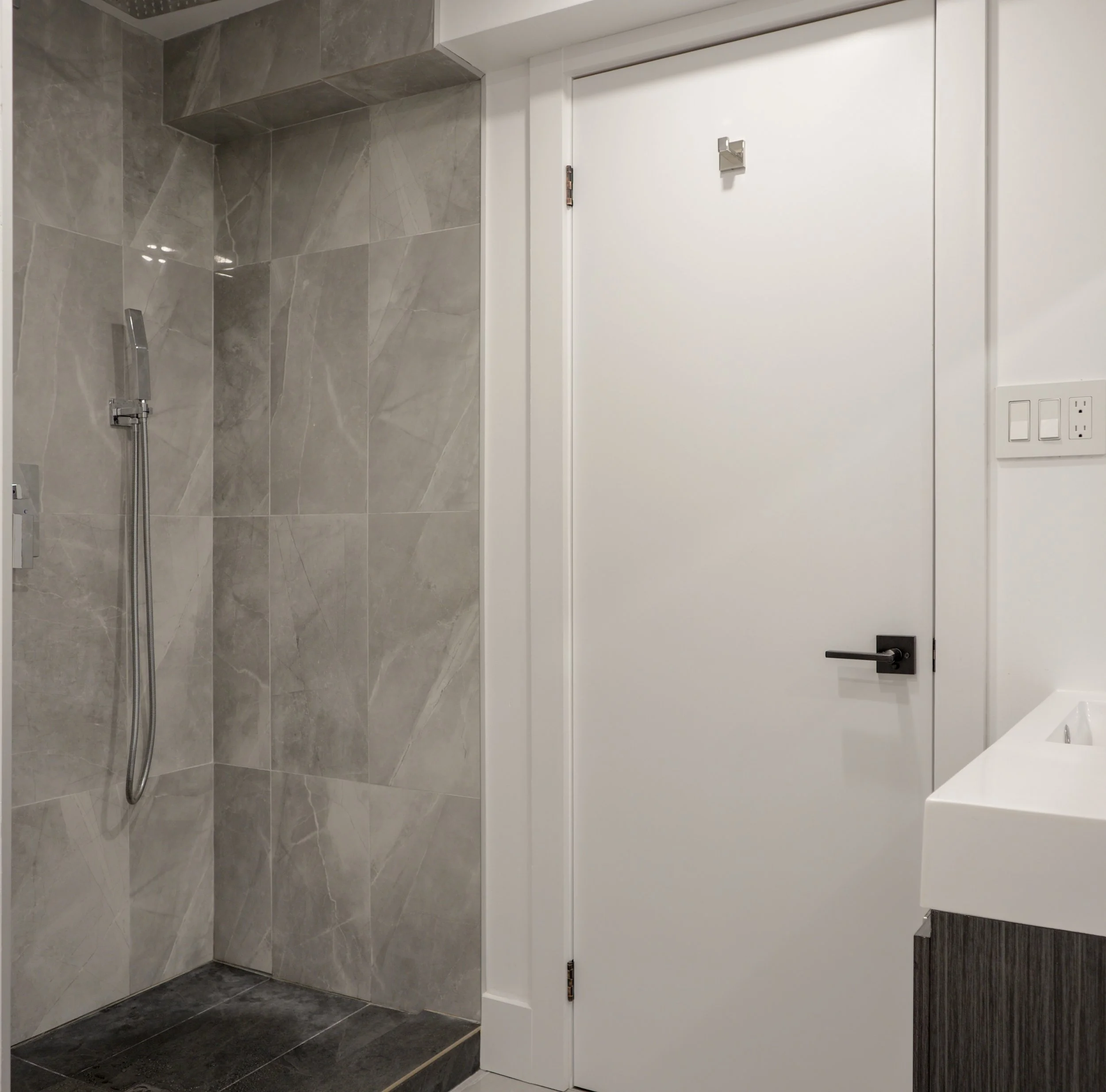 Modern basement bathroom with grey porcelain tile shower, white vanity, black fixtures, and dual-entry door in Vaughan, Ontario renovation.