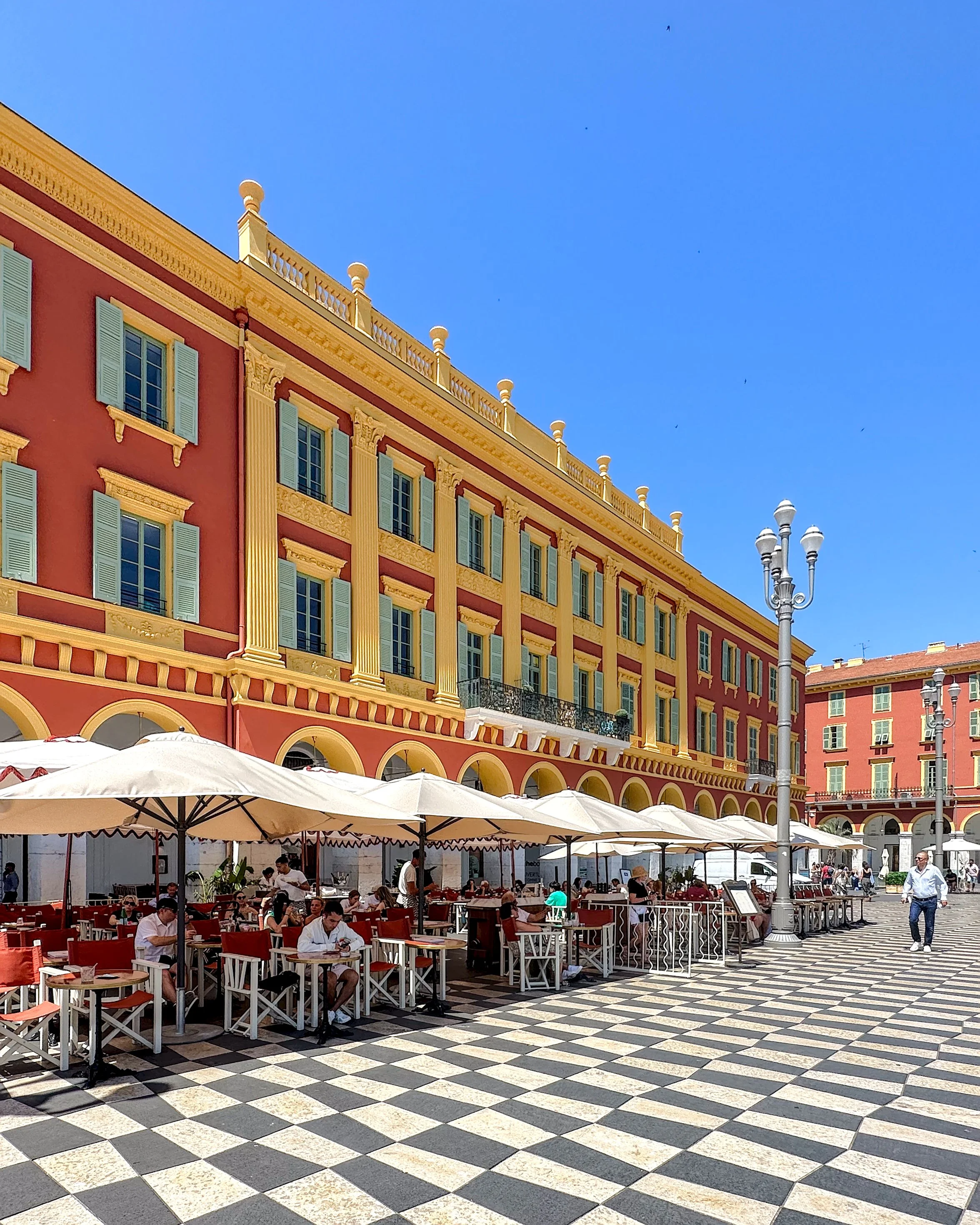 Place Masséna in Nice, France with outdoor café seating, red and yellow buildings, and black-and-white patterned square