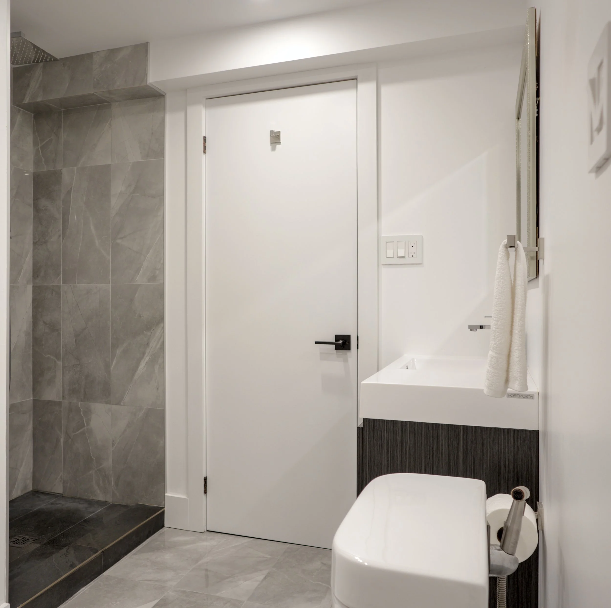 Modern basement bathroom with grey porcelain tile shower, white vanity, black fixtures, and dual-entry door in Vaughan, Ontario renovation.