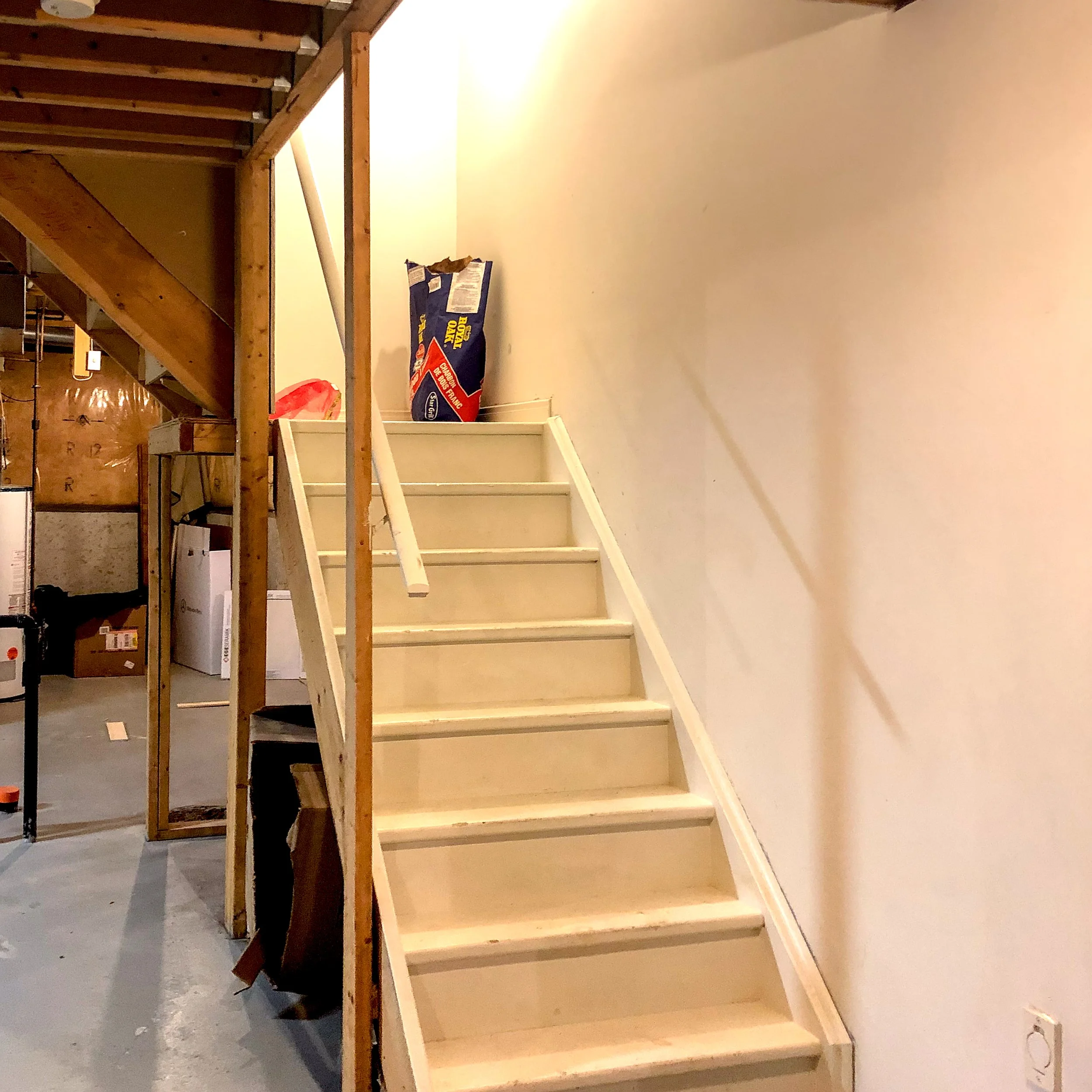 Old builder-grade basement staircase with narrow white-painted steps before renovation
