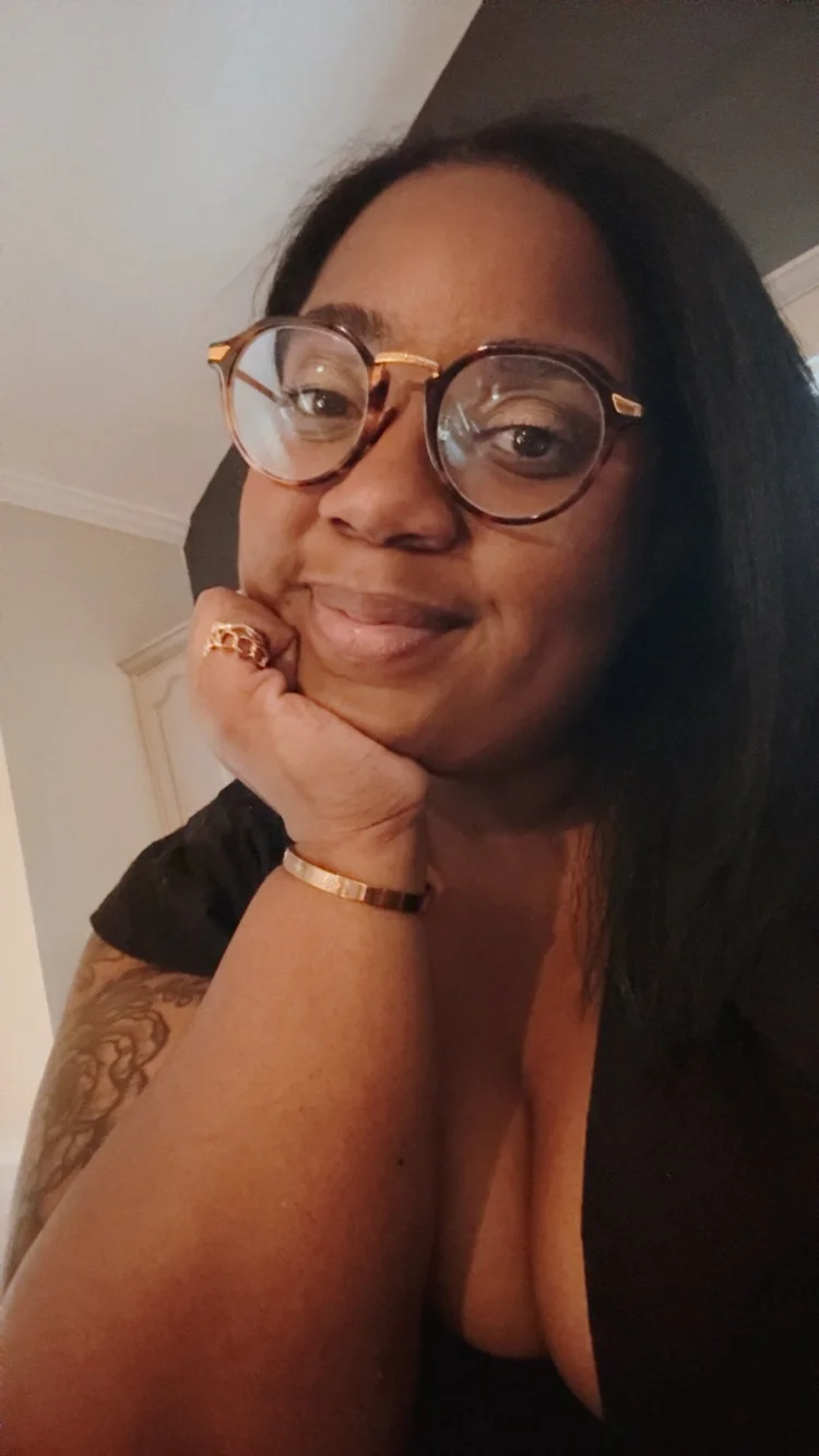 Thobi in round glasses resting her chin on her hand