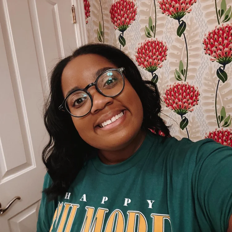 Thobi smiling in a green HAPPY t-shirt in front of pink floral wallpaper