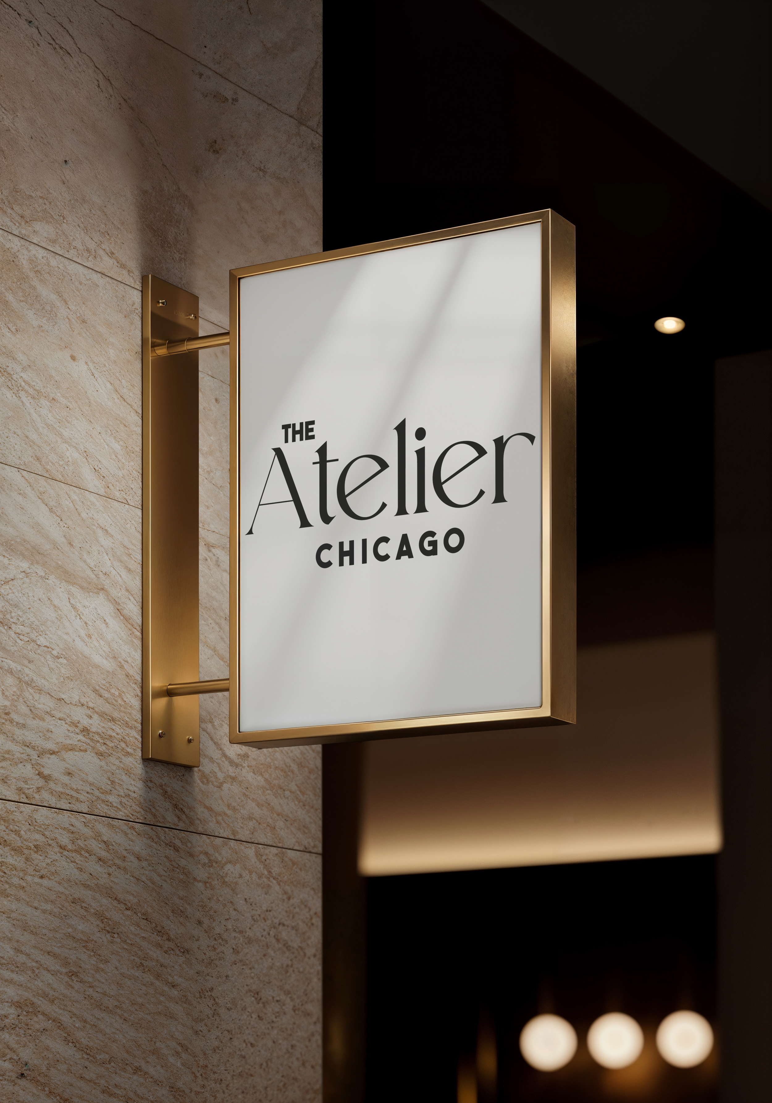 Lightbox sign for 'The Atelier Chicago' mounted on a beige stone wall, with warm lighting in an indoor setting.