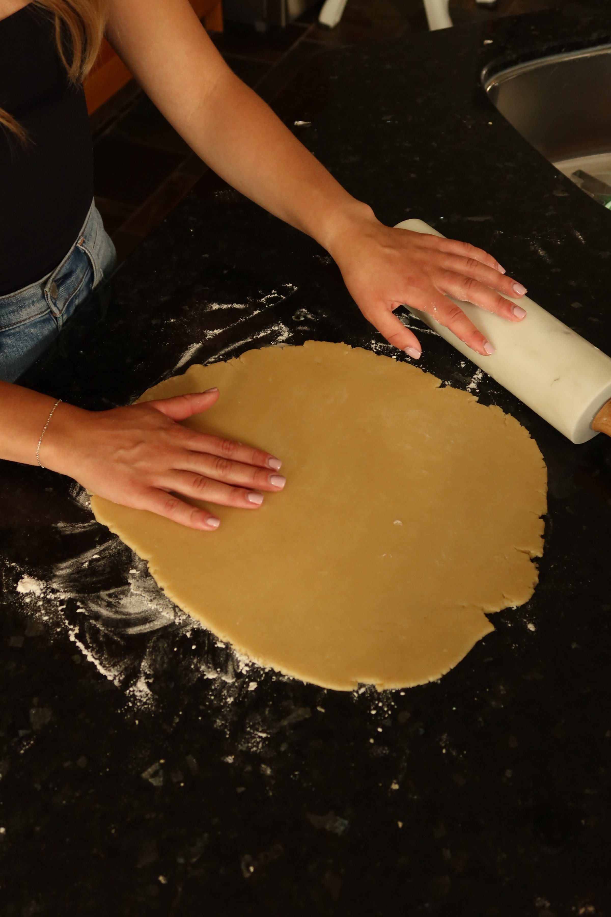 Person rolling out cookie dough with a rolling pin on a black countertop.