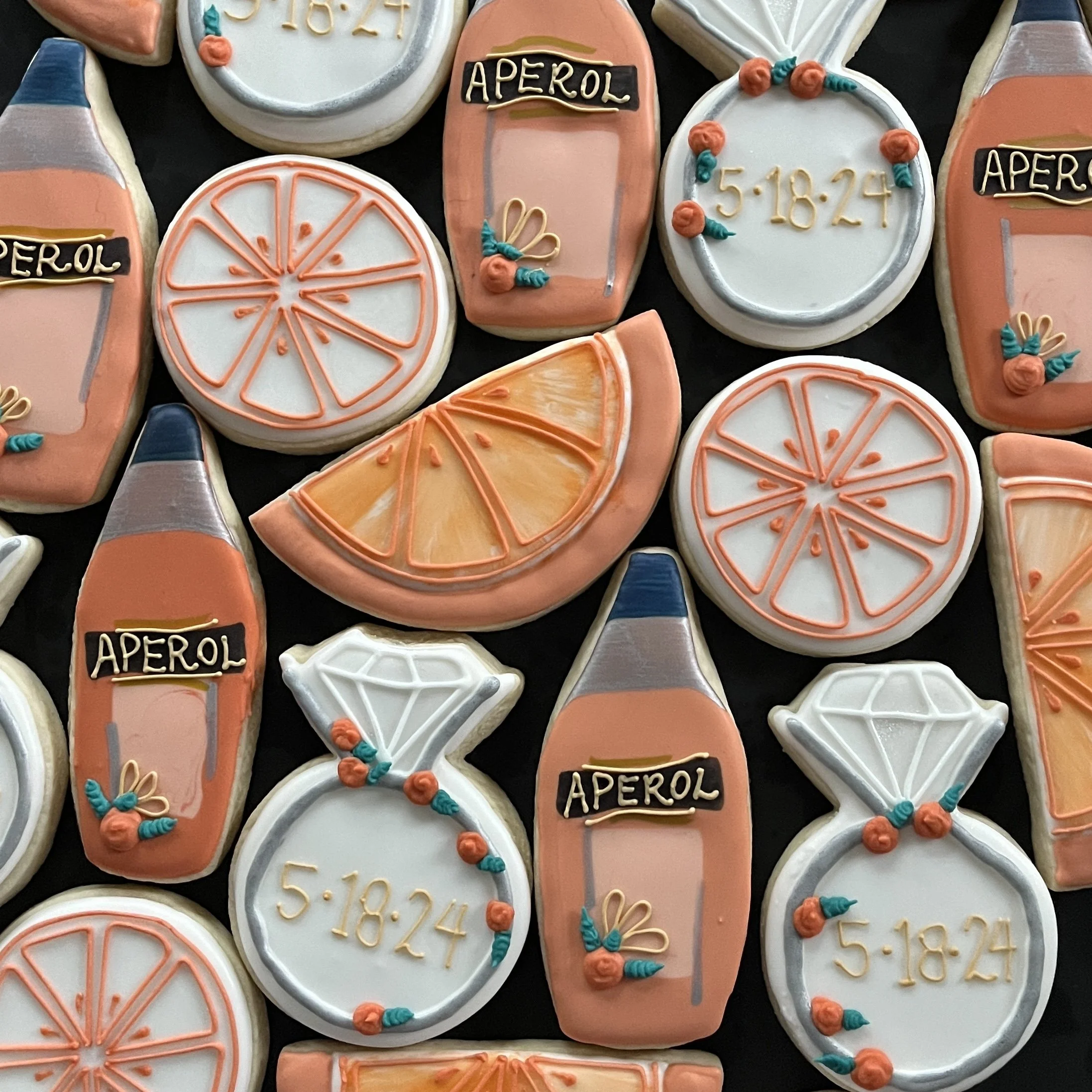 Decorated cookies shaped like orange slices, cocktail bottles labeled 'Aperol' with floral embellishments, and small bottles with the date 5:18:24, in pastel orange, white, and blue colors.