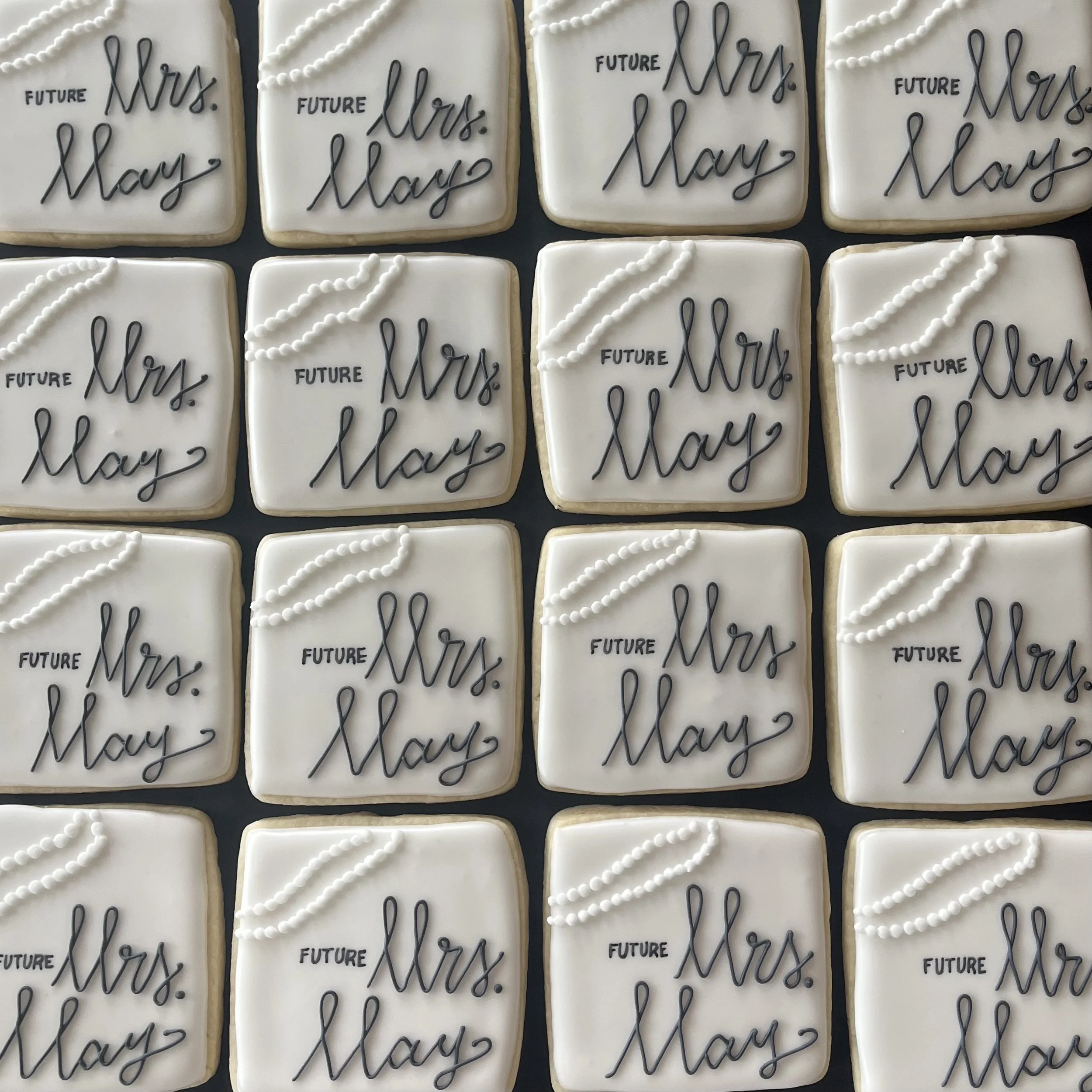 Decorated cookies with white icing, each featuring the words 'Future Mrs. May' written in black icing and a pearl-like pattern in the top left corner.