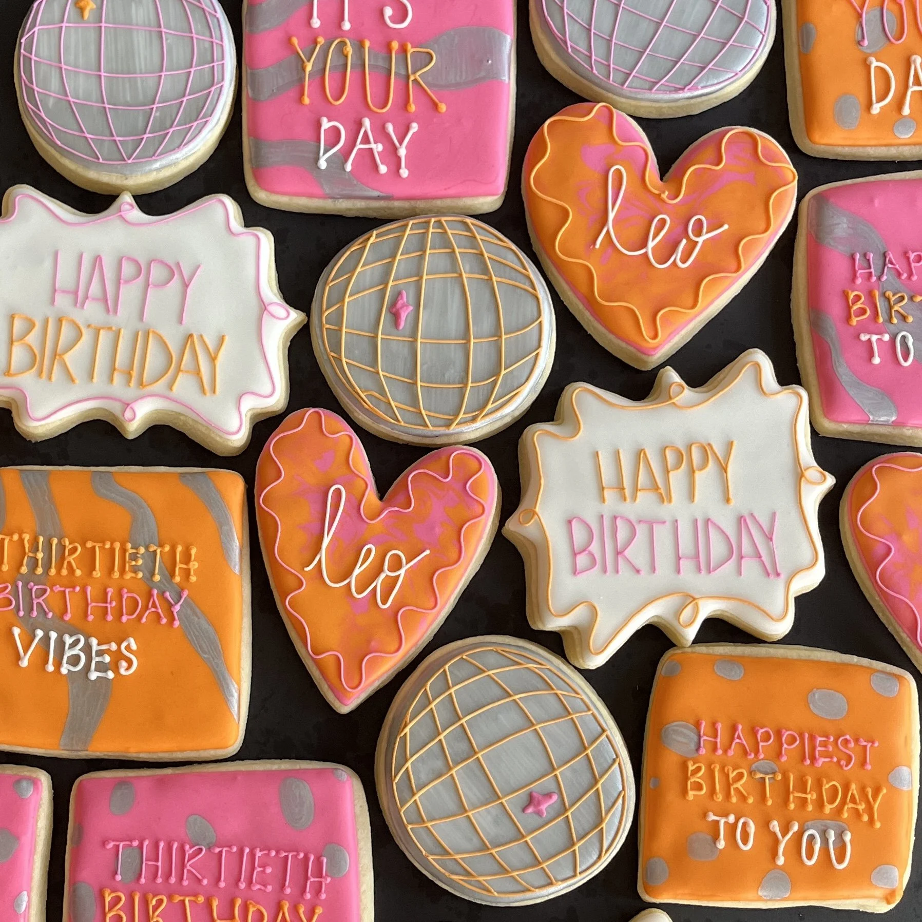 Decorated birthday cookies with pink, orange, and gray icing, message reading 'Happy Birthday,' 'Thirtieth birthday,' and 'Happiest birthday to you,' featuring globe and heart shapes with colorful designs.