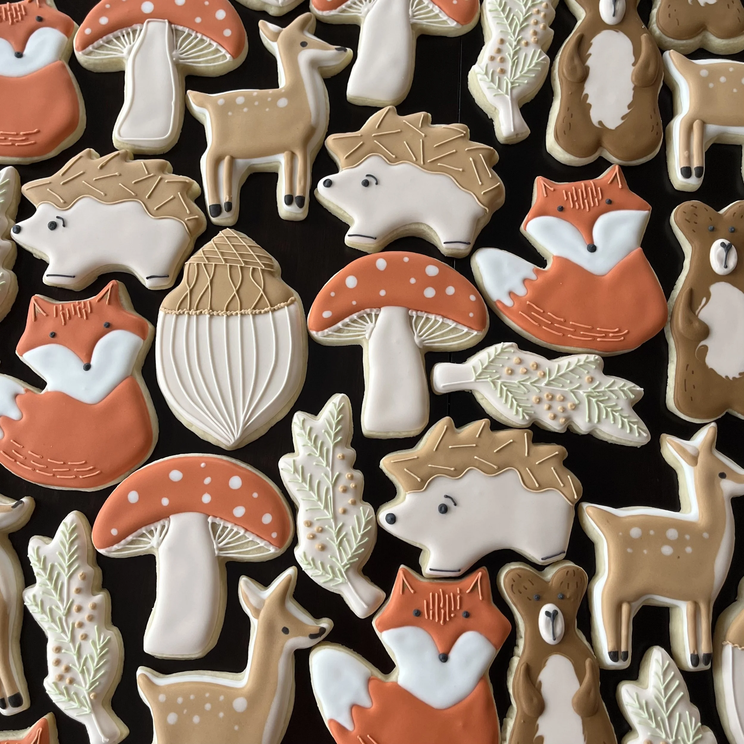 Decorative cookies shaped like foxes, deer, hedgehogs, mushrooms, leaves, and acorns with detailed icing design in fall colors