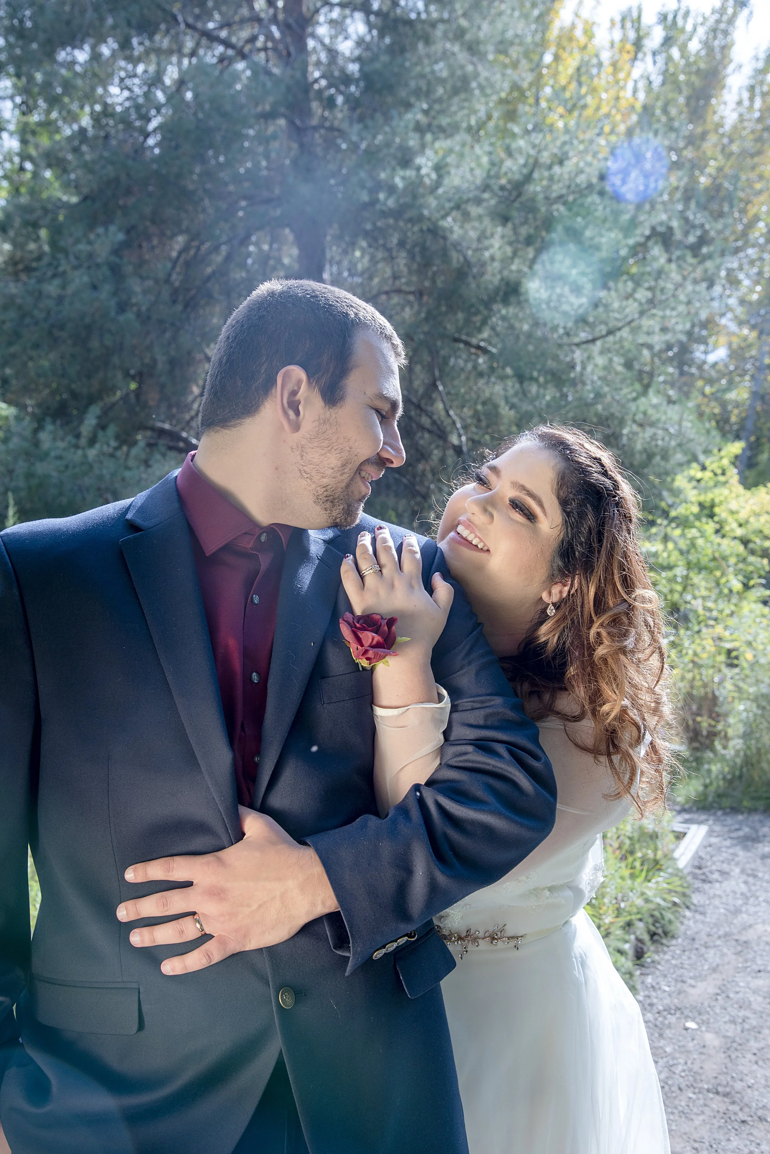 A couple dressed in wedding attire sharing a joyful moment outdoors with greenery in the background.