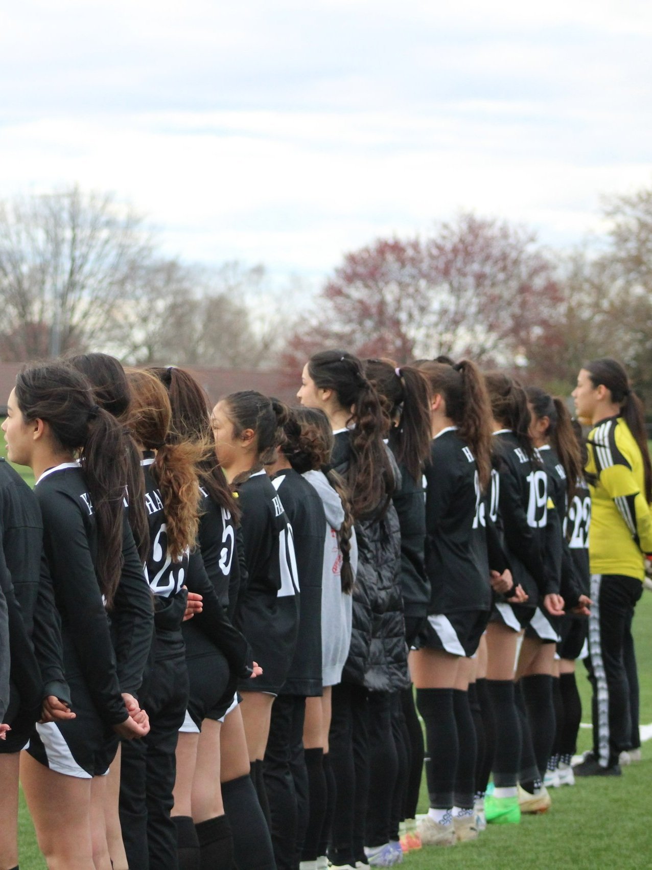 Line of female soccer players standing on the field during a game. From Harvard Illinois, soccer program for Harvard High School, in McHenry County. Athletic session and portraits of soccer athletic team.