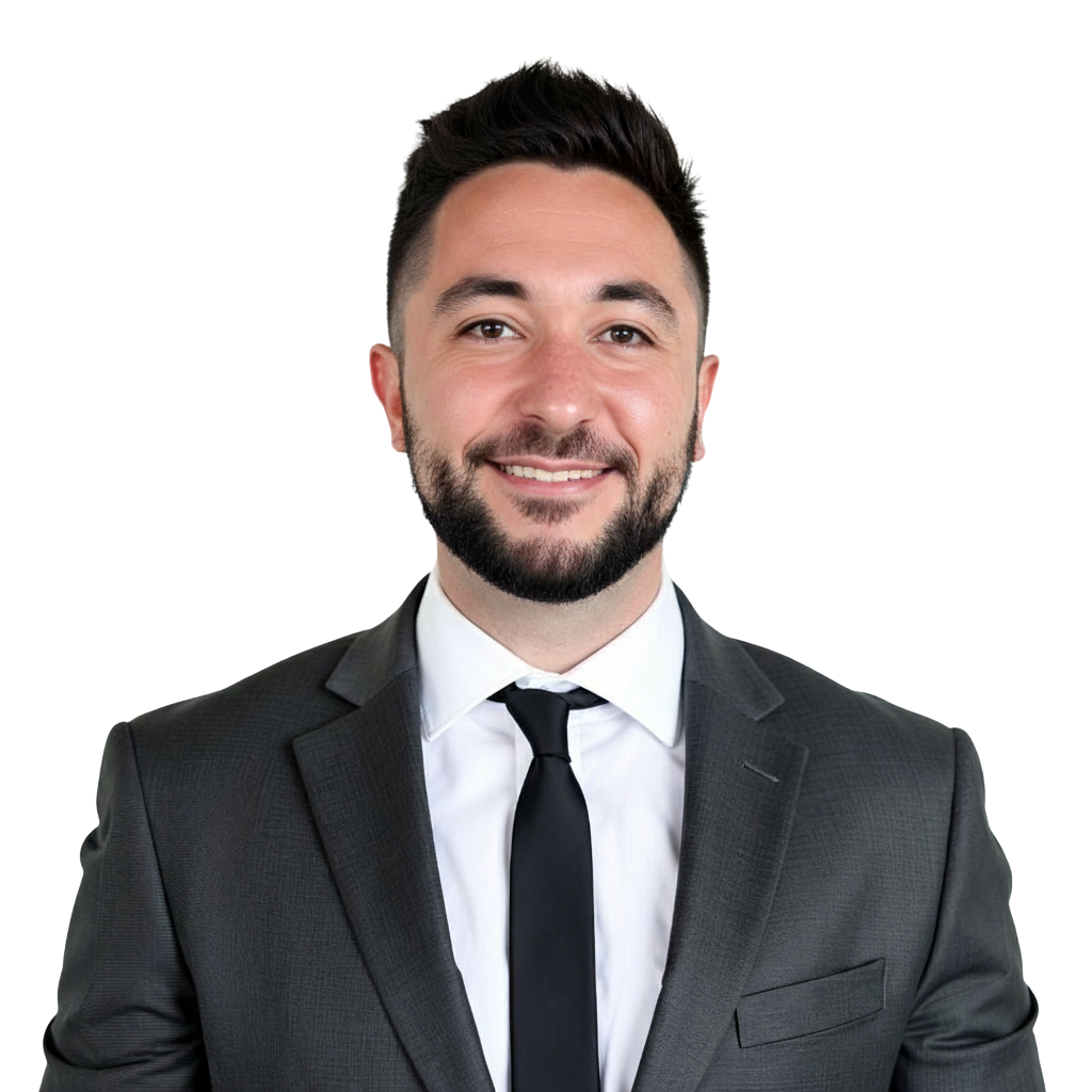 A smiling man in a black suit, white shirt, and black tie, with short dark hair and a beard.