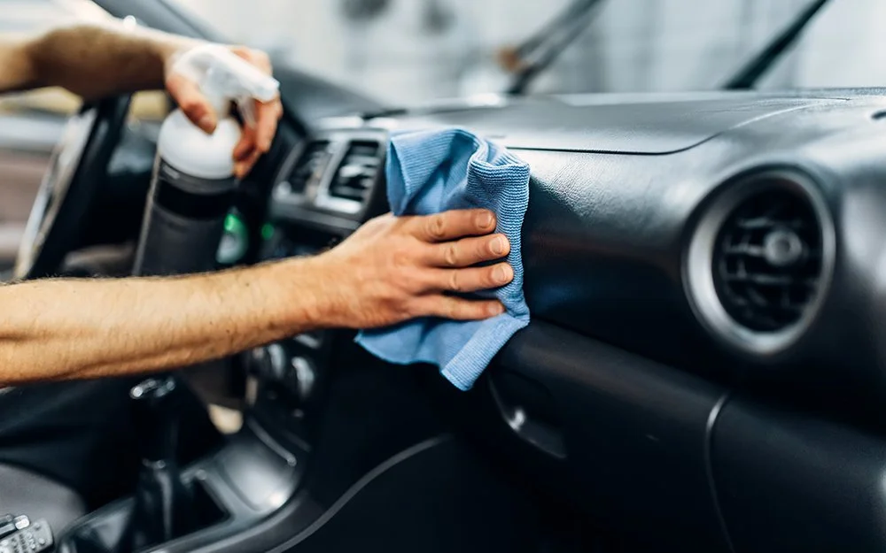 Person cleaning the dashboard of a car with a blue cloth.
