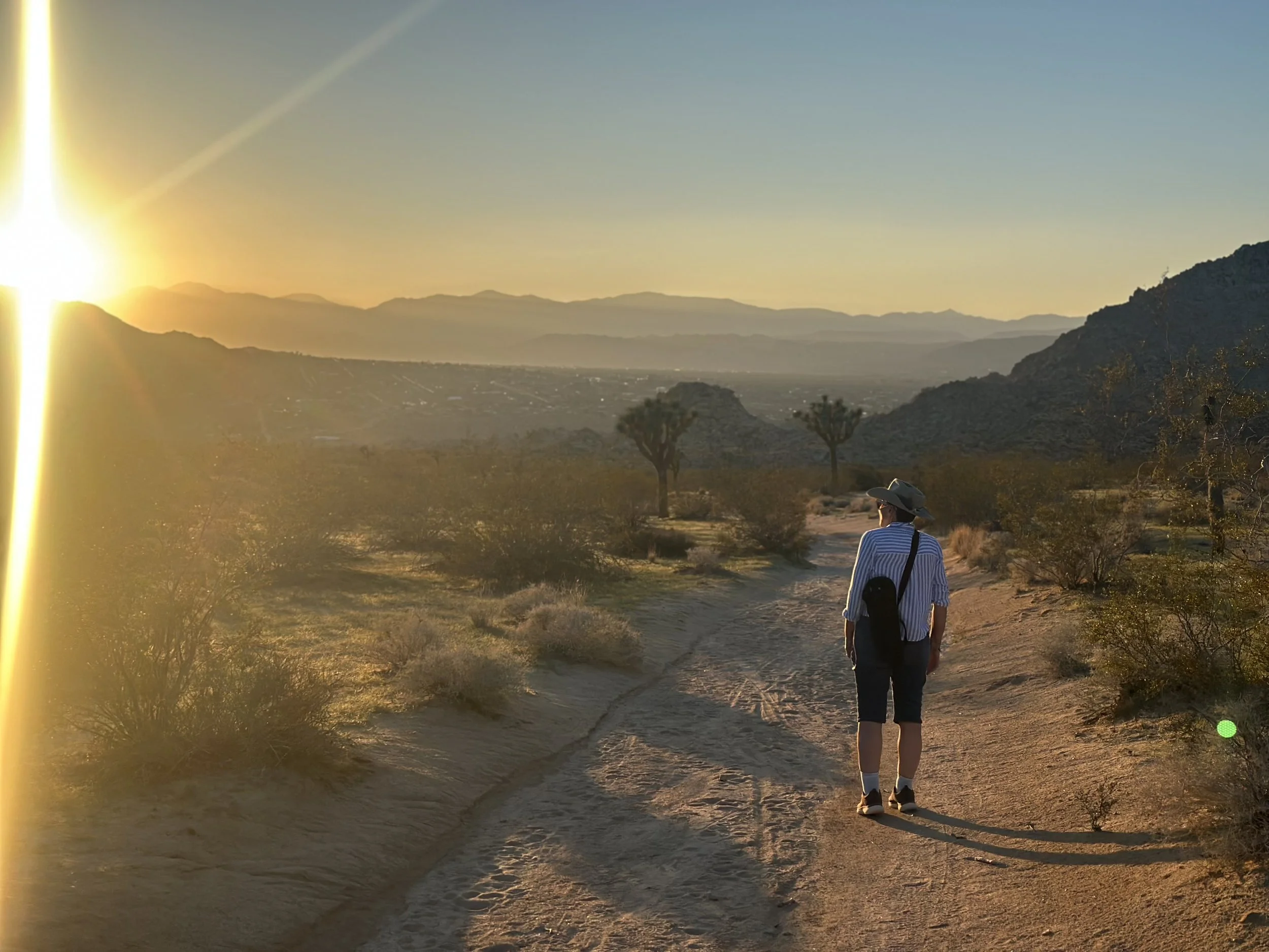 Jennifer Evridge walking a desert trail at sunrise among Joshua trees, mountains in the distance.