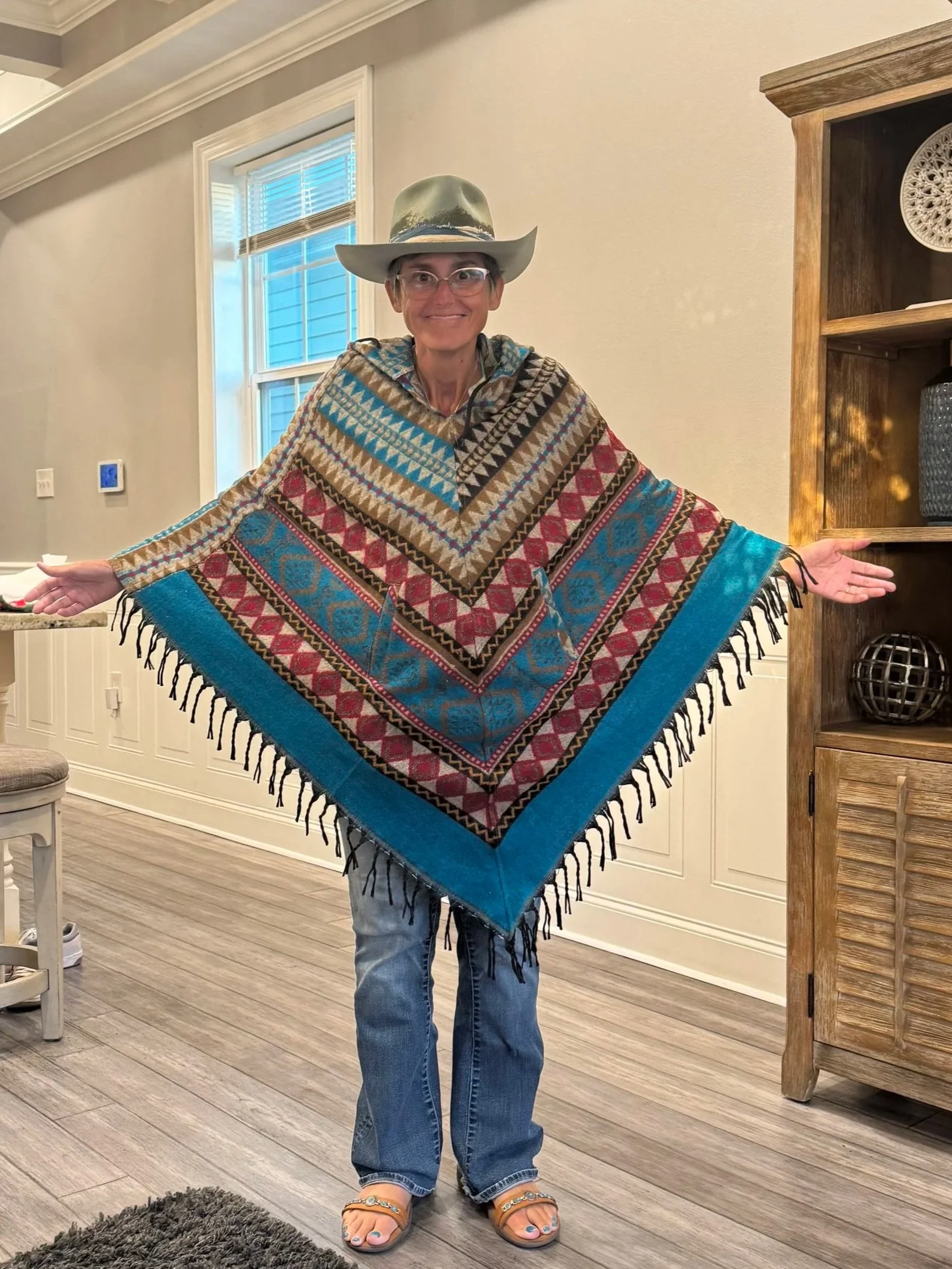 Jennifer Evridge smiling with arms outstretched, wearing a patterned poncho and hat