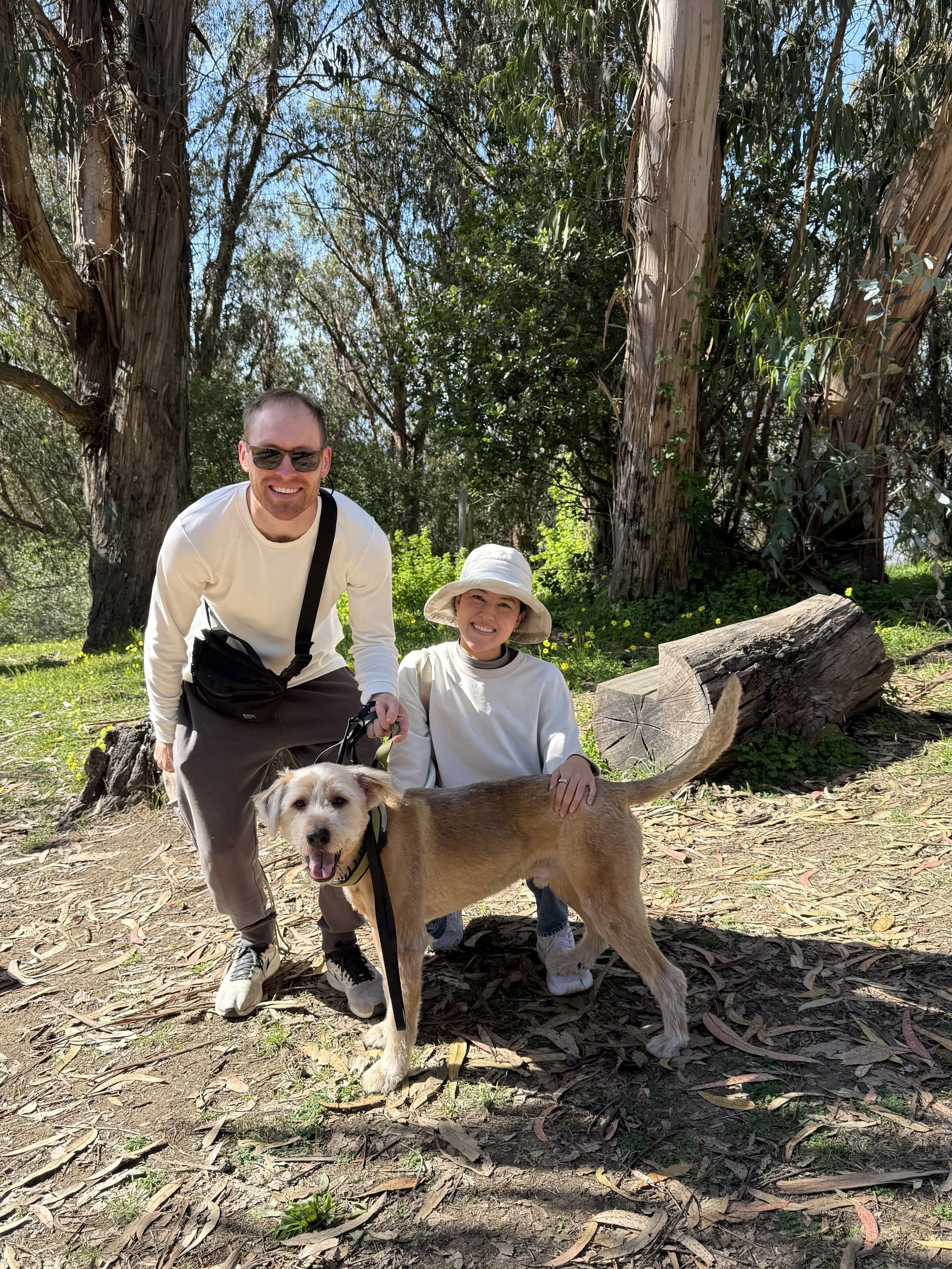 A man, woman, and dog posing in a woody area