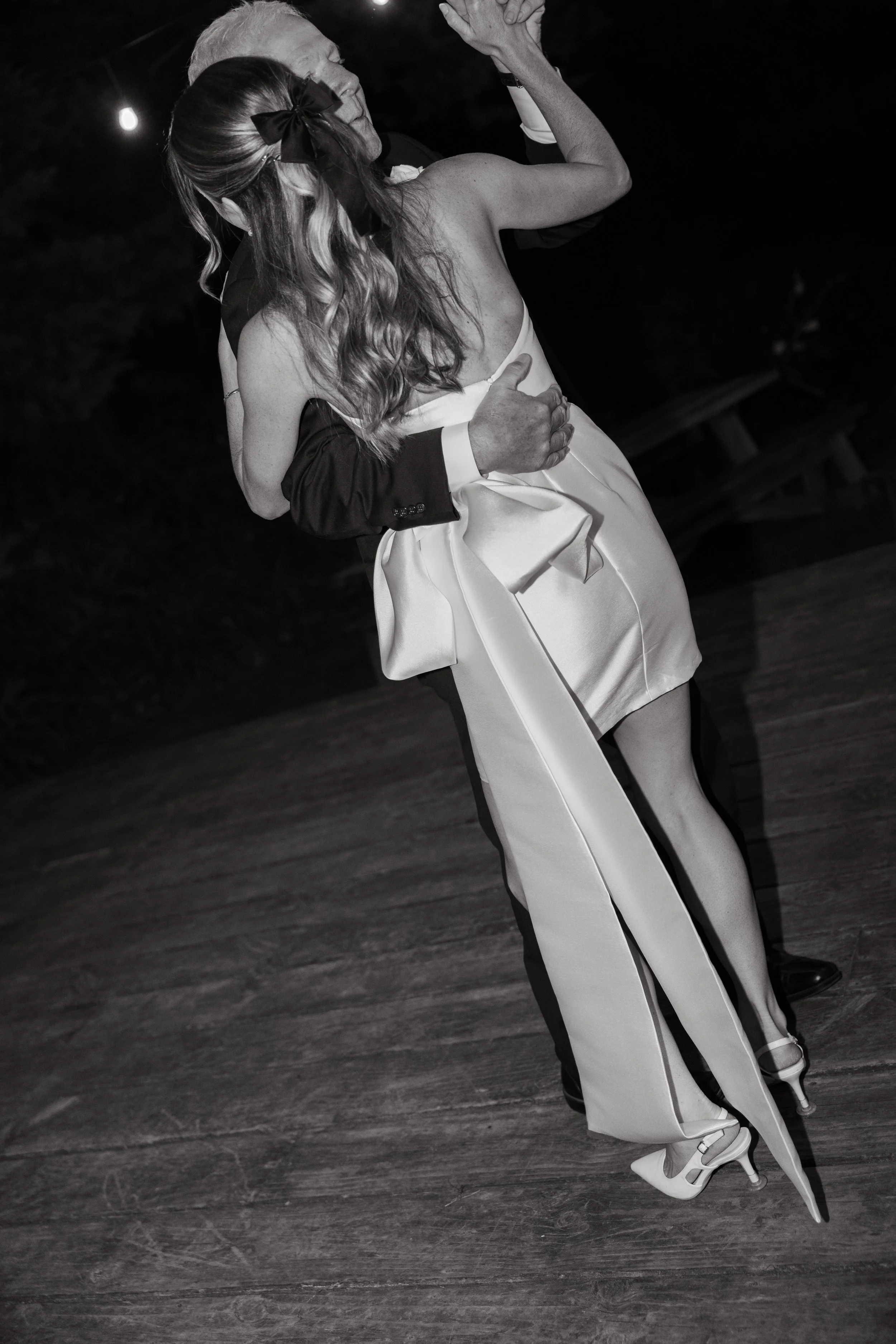 A couple dancing closely at a wedding reception, with the woman in a strapless dress and the man in a suit, on a wooden dance floor.