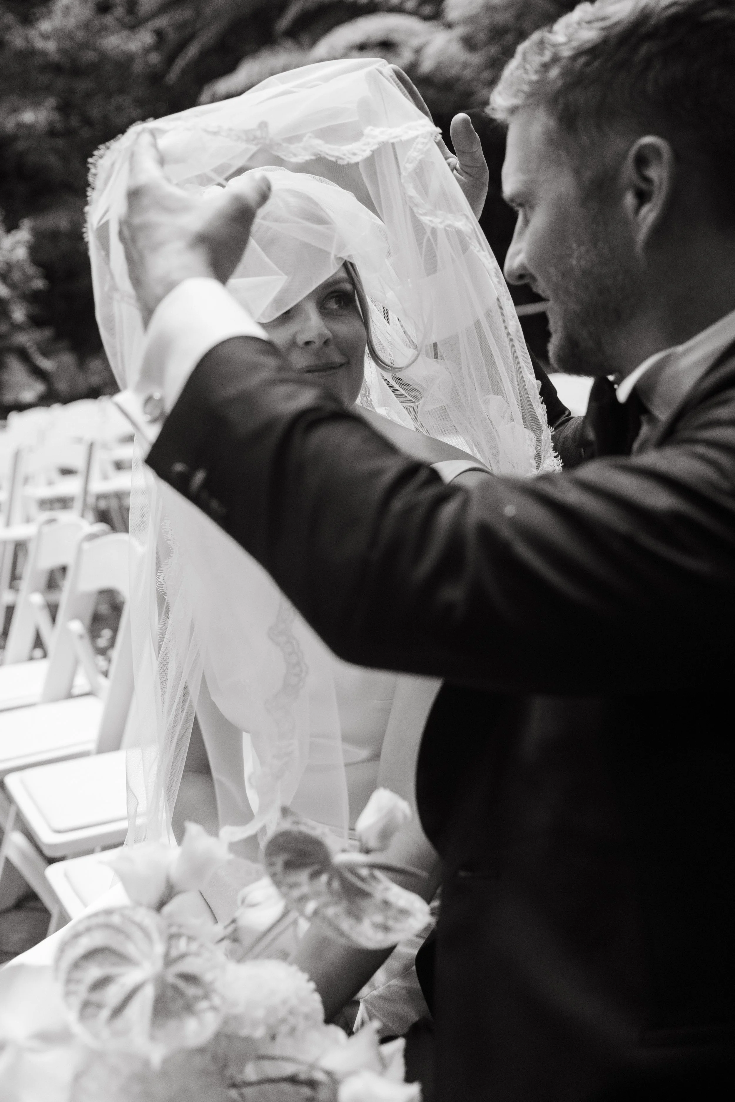A groom adjusting a bride's veil during a wedding ceremony outdoors.