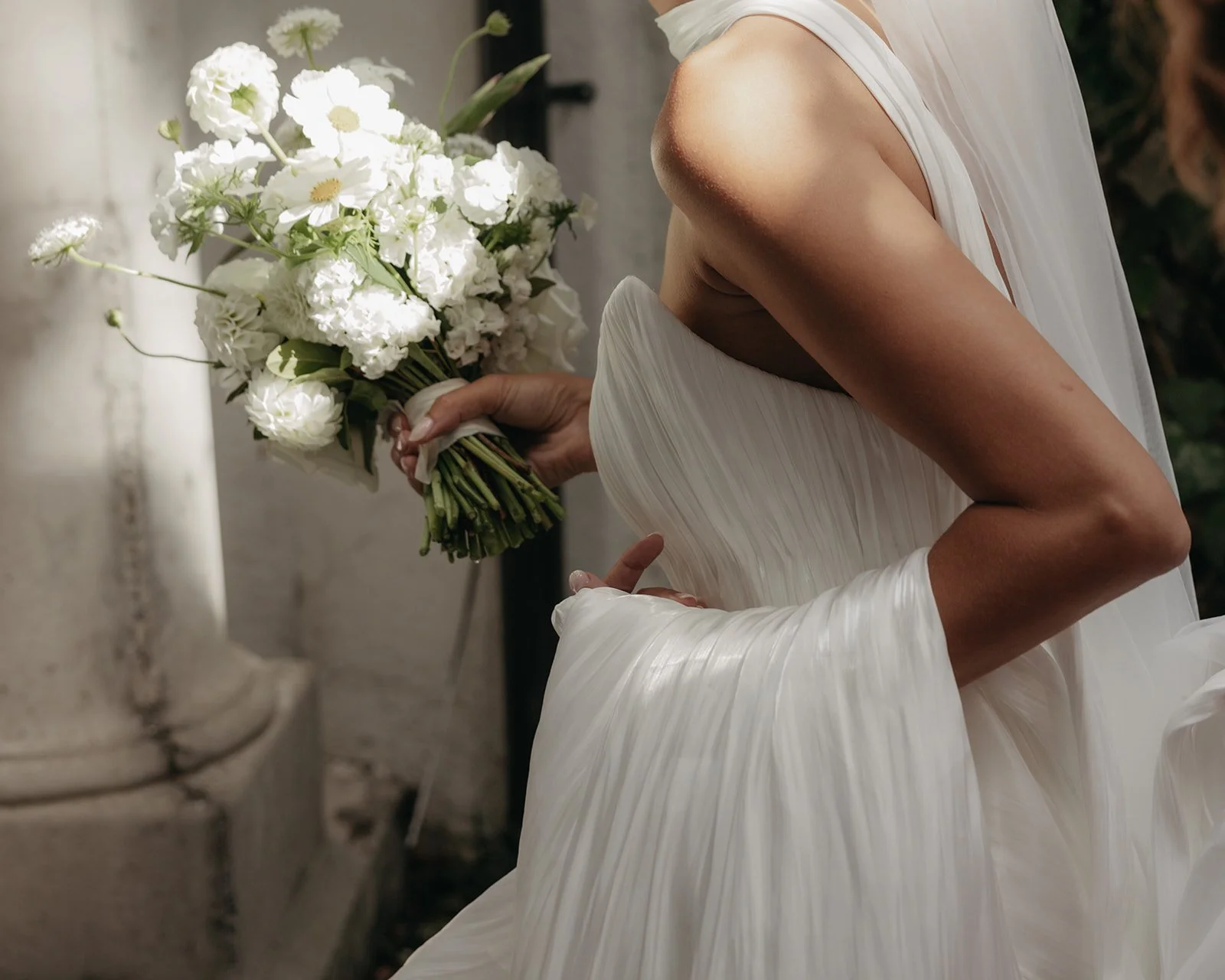 Close-up of a woman in a white dress holding a bouquet of white flowers.